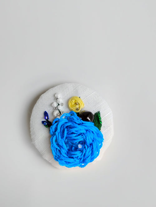 Decorative blue flower brooch on white textured background