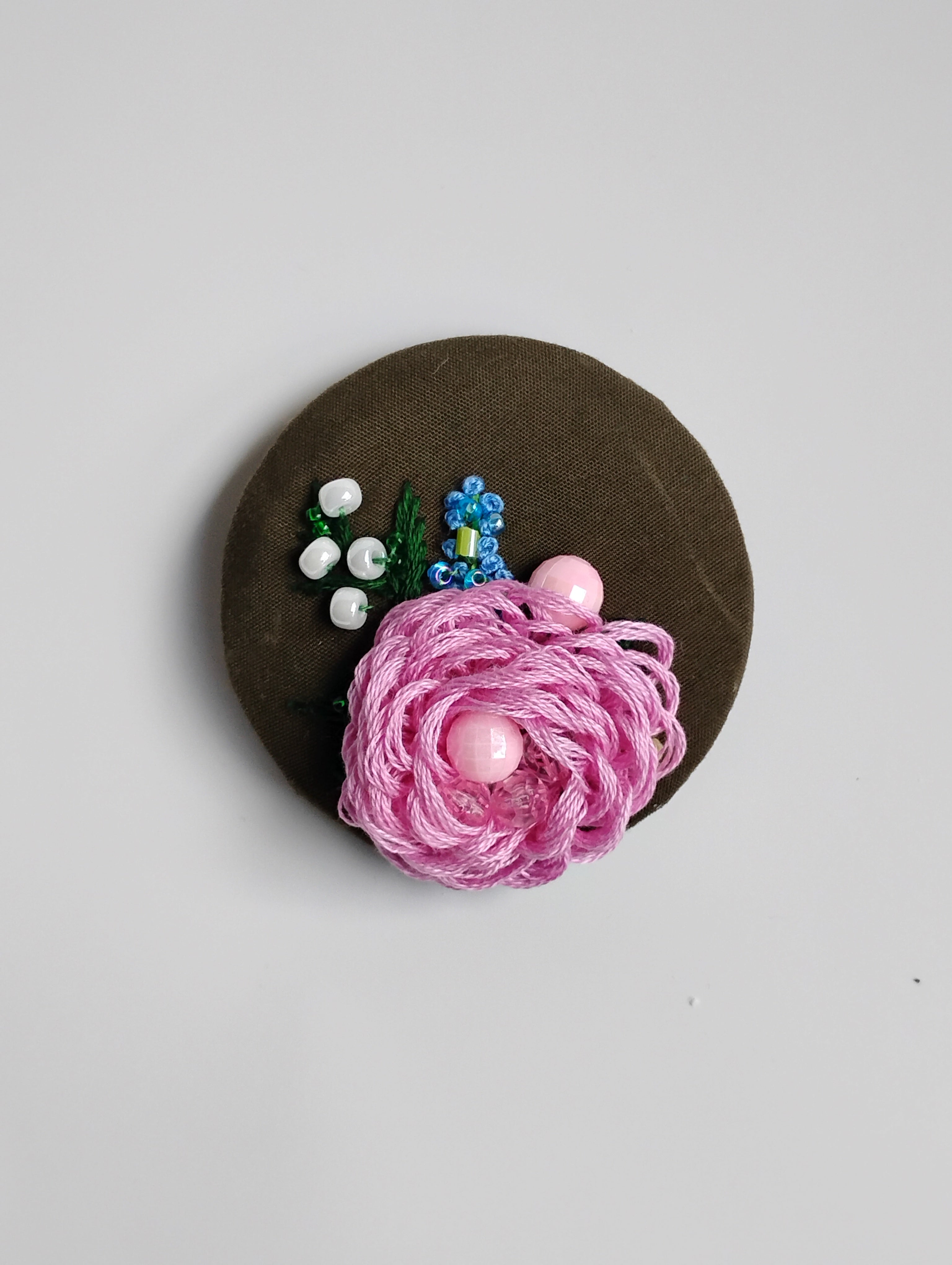 Decorative pink flower brooch on olive background