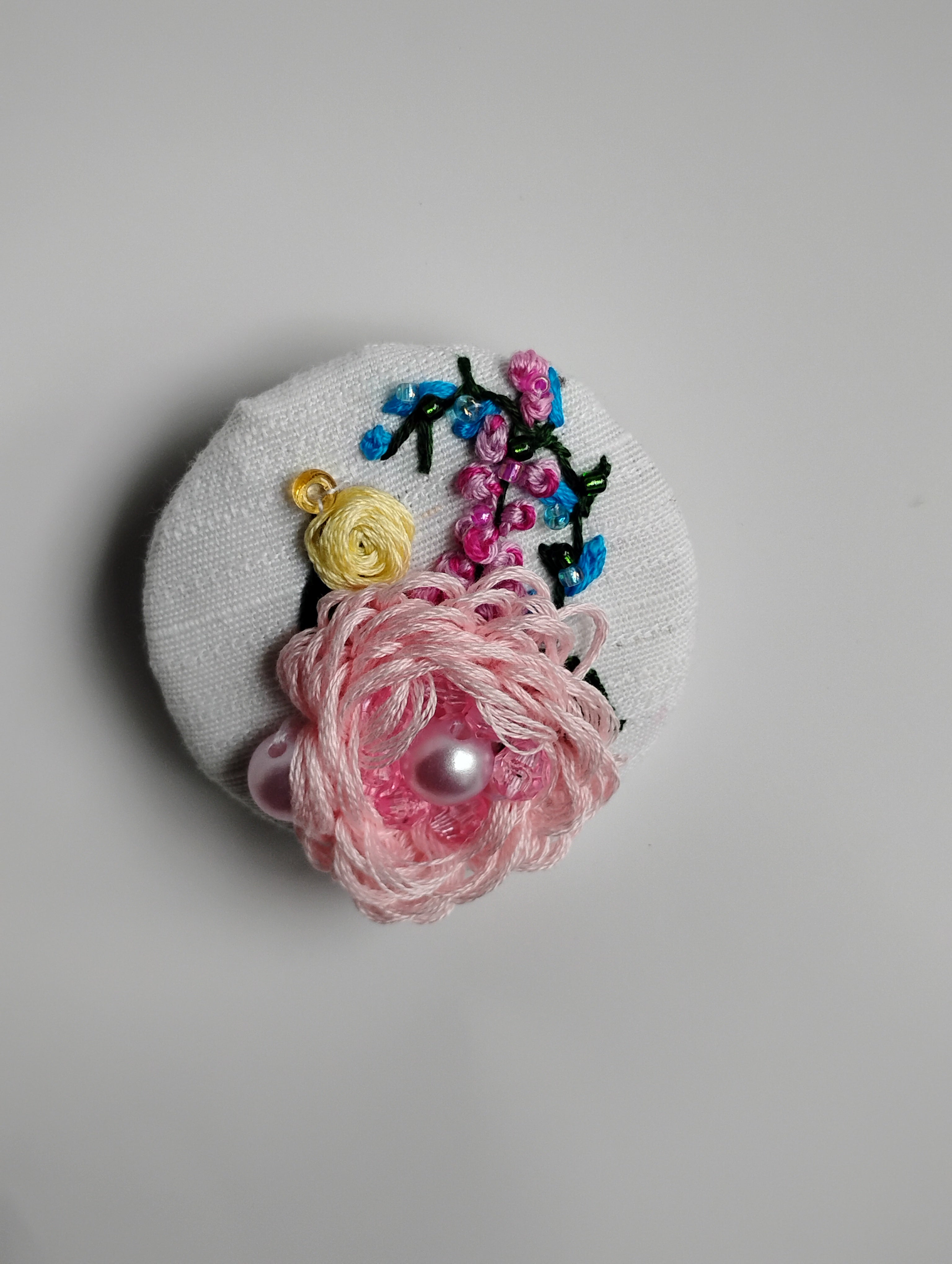 Decorative pink flower brooch on white textured background
