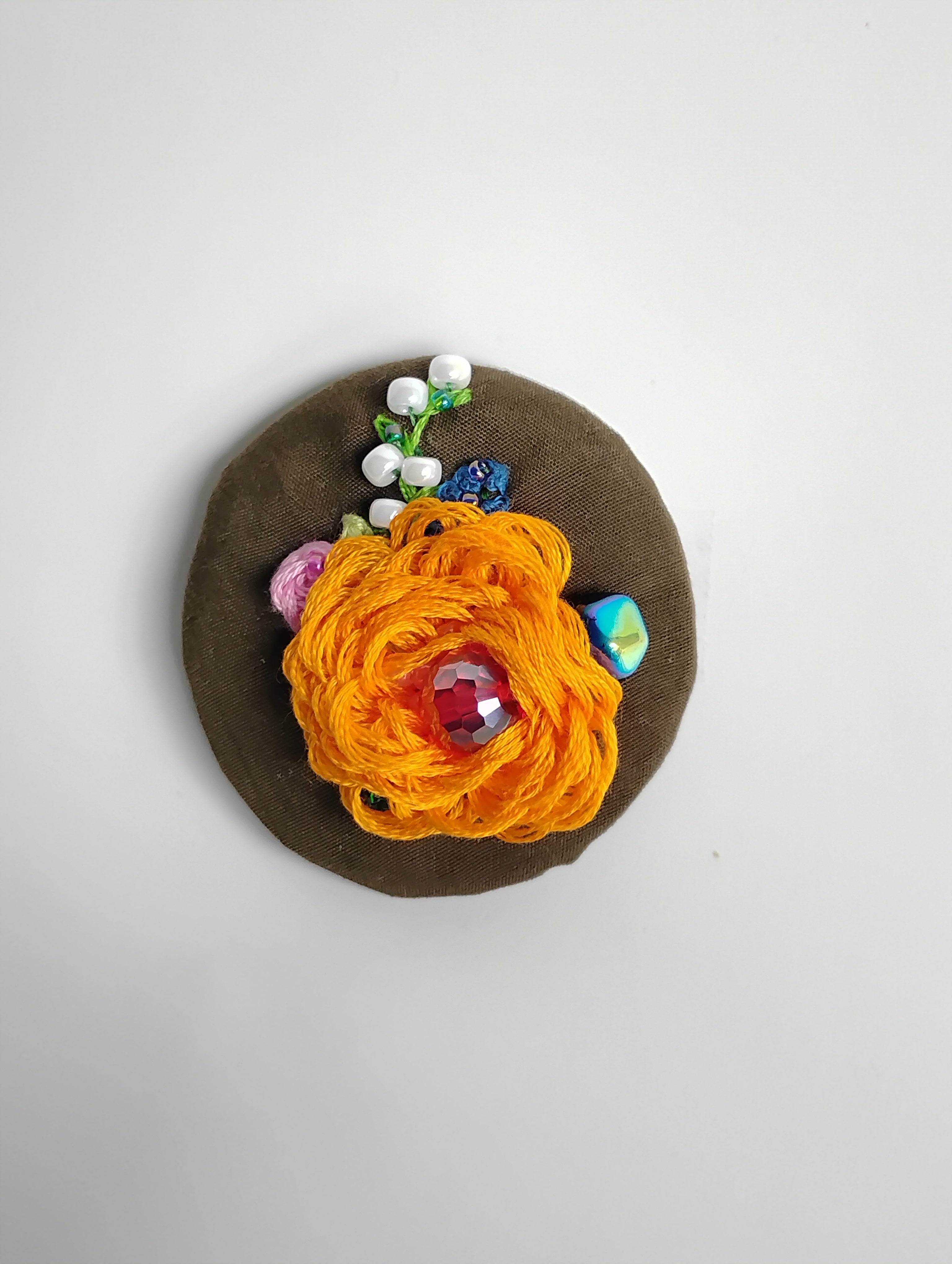 Decorative orange flower brooch on olive background