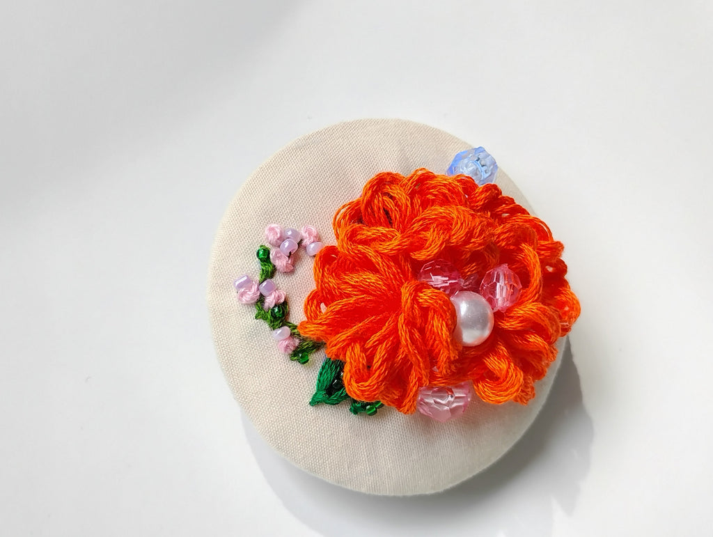 Decorative orange flower brooch on cream background