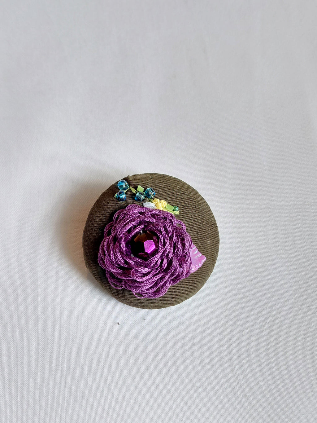 Decorative purple flower brooch on olive background