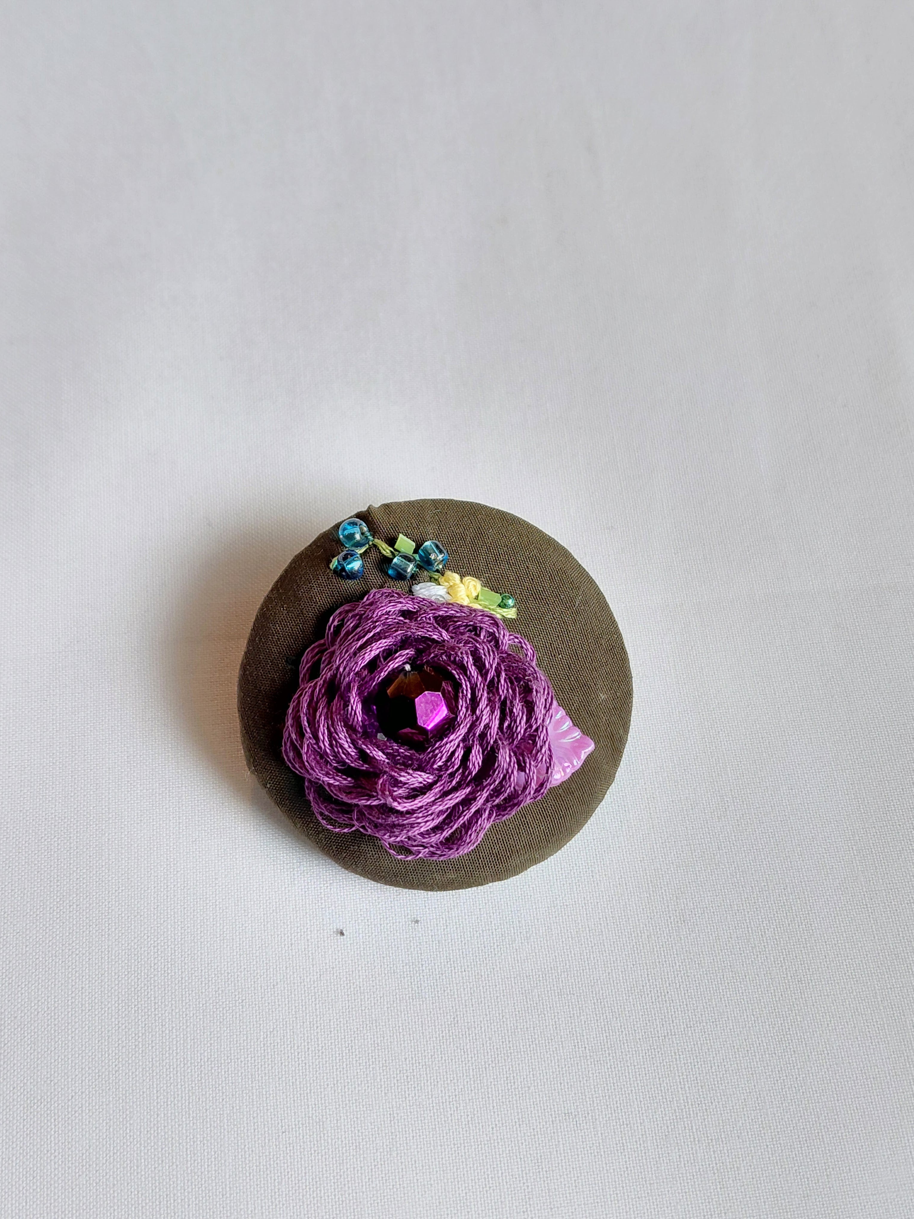 Decorative purple flower brooch on olive background