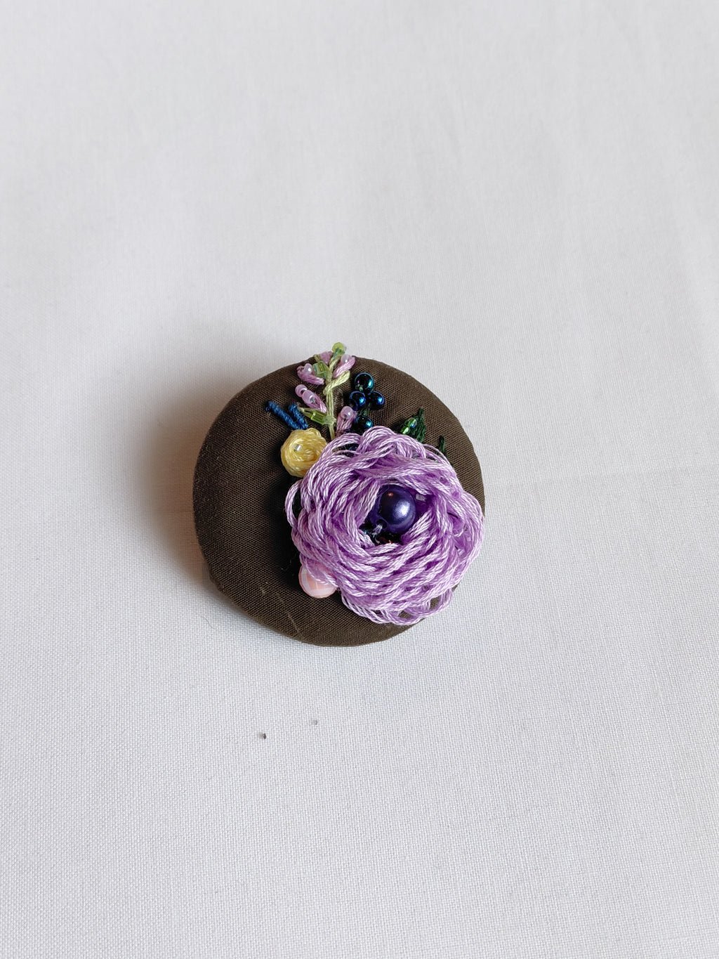 Decorative purple flower brooch on olive background