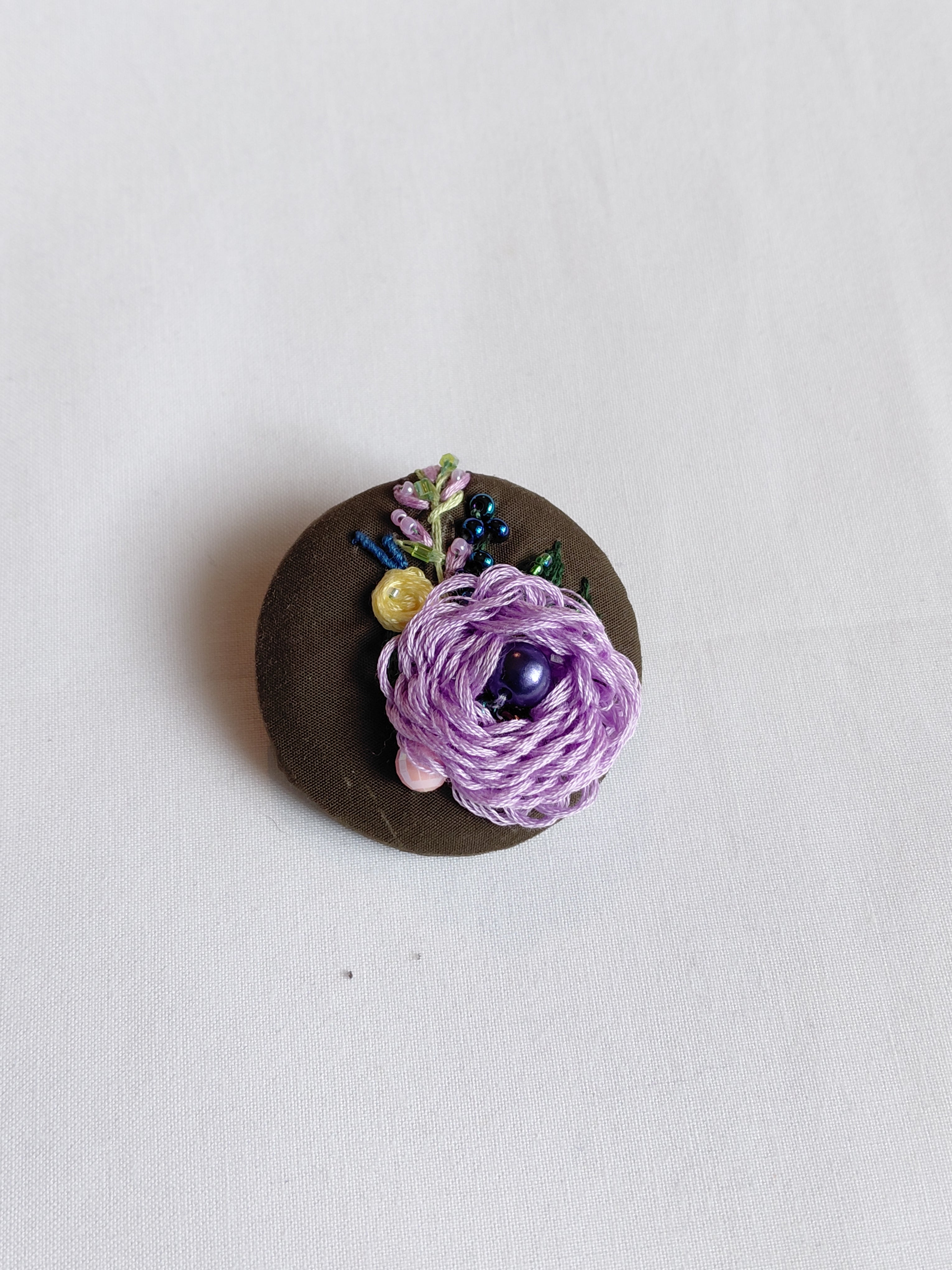 Decorative purple flower brooch on olive background