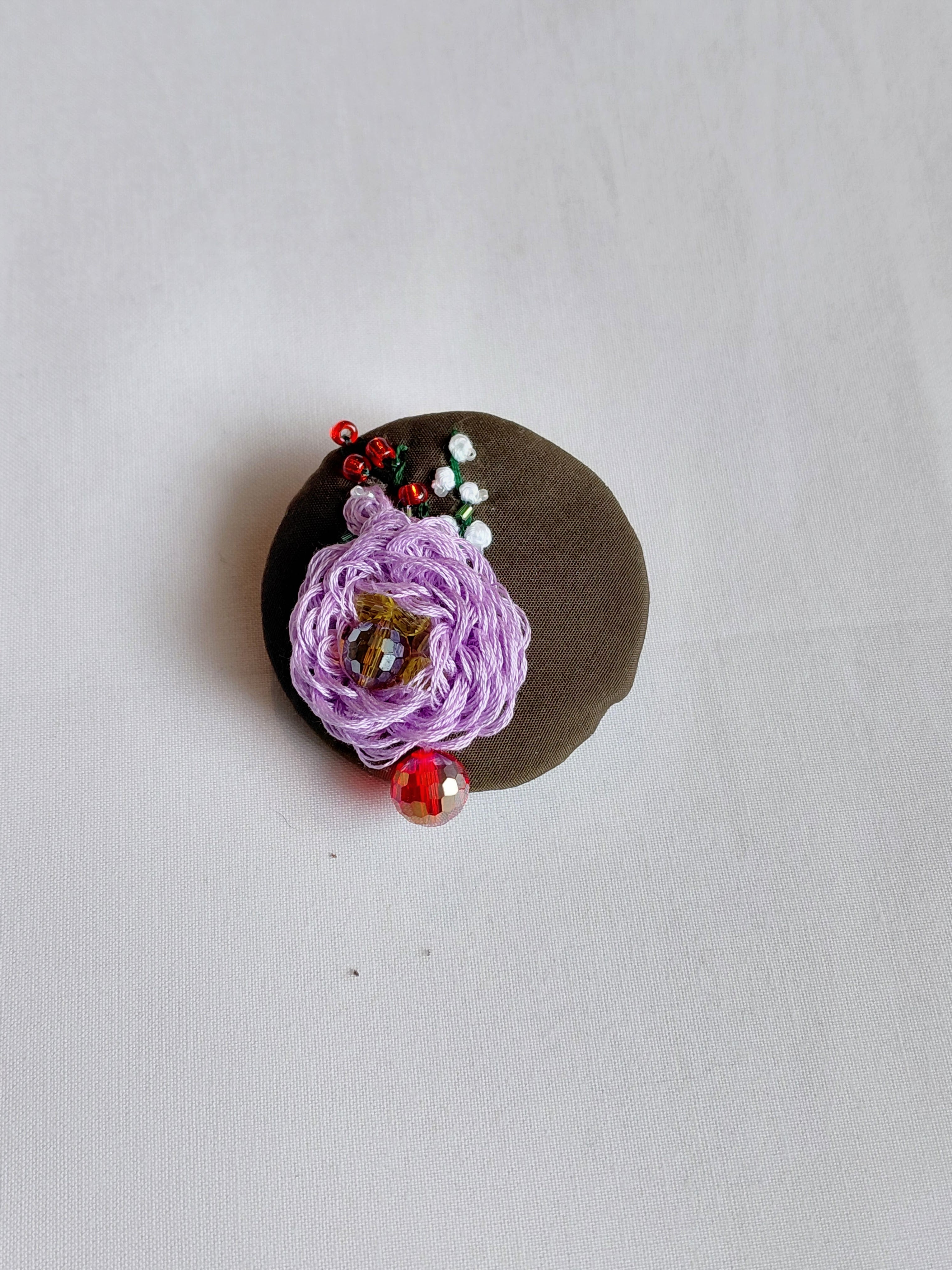 Decorative purple flower brooch on olive background