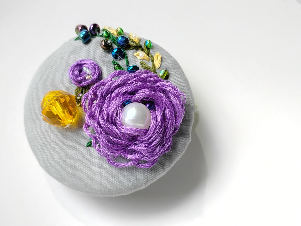 Decorative purple flower brooch on grey background