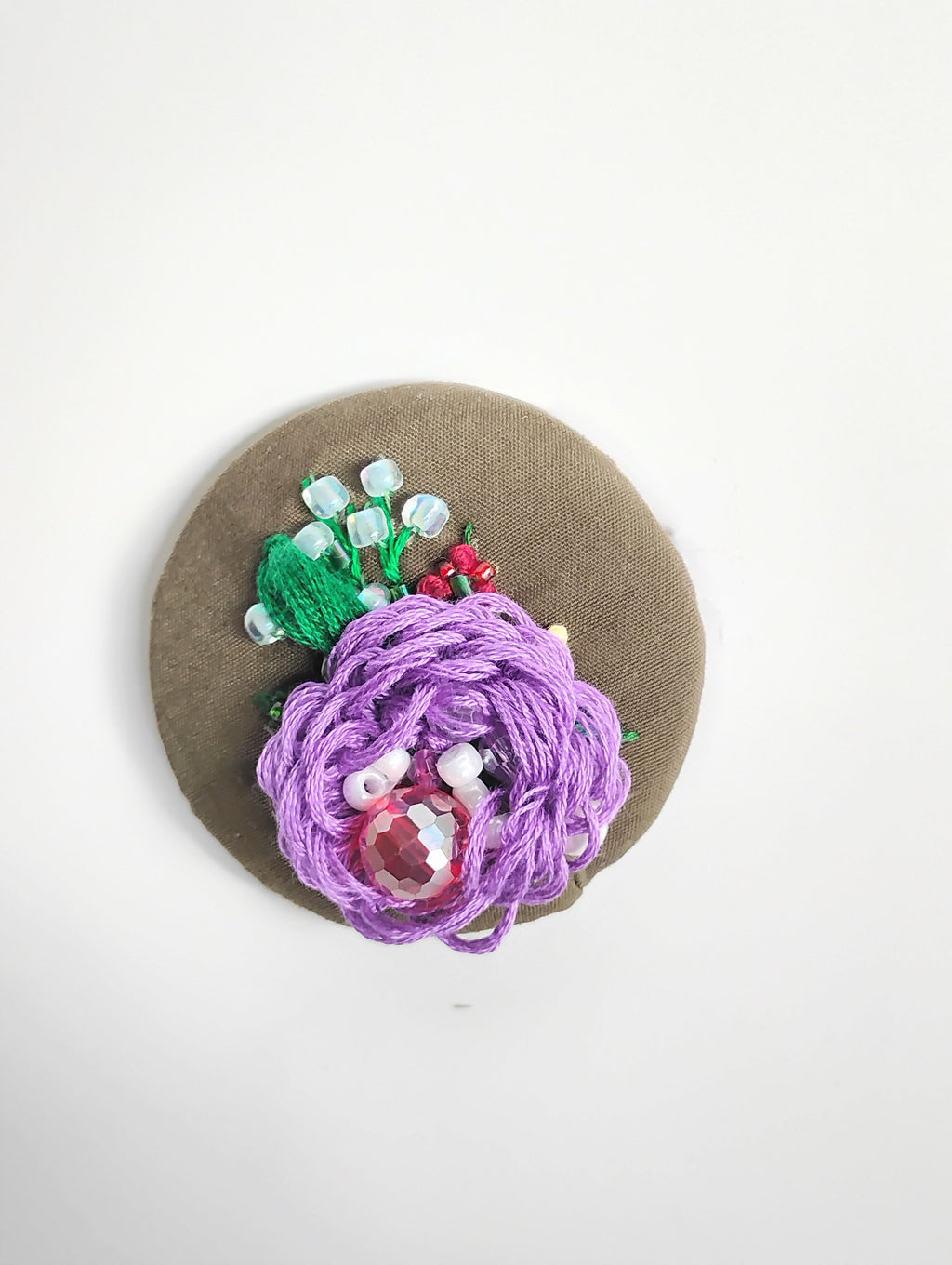 Decorative purple flower brooch on olive background