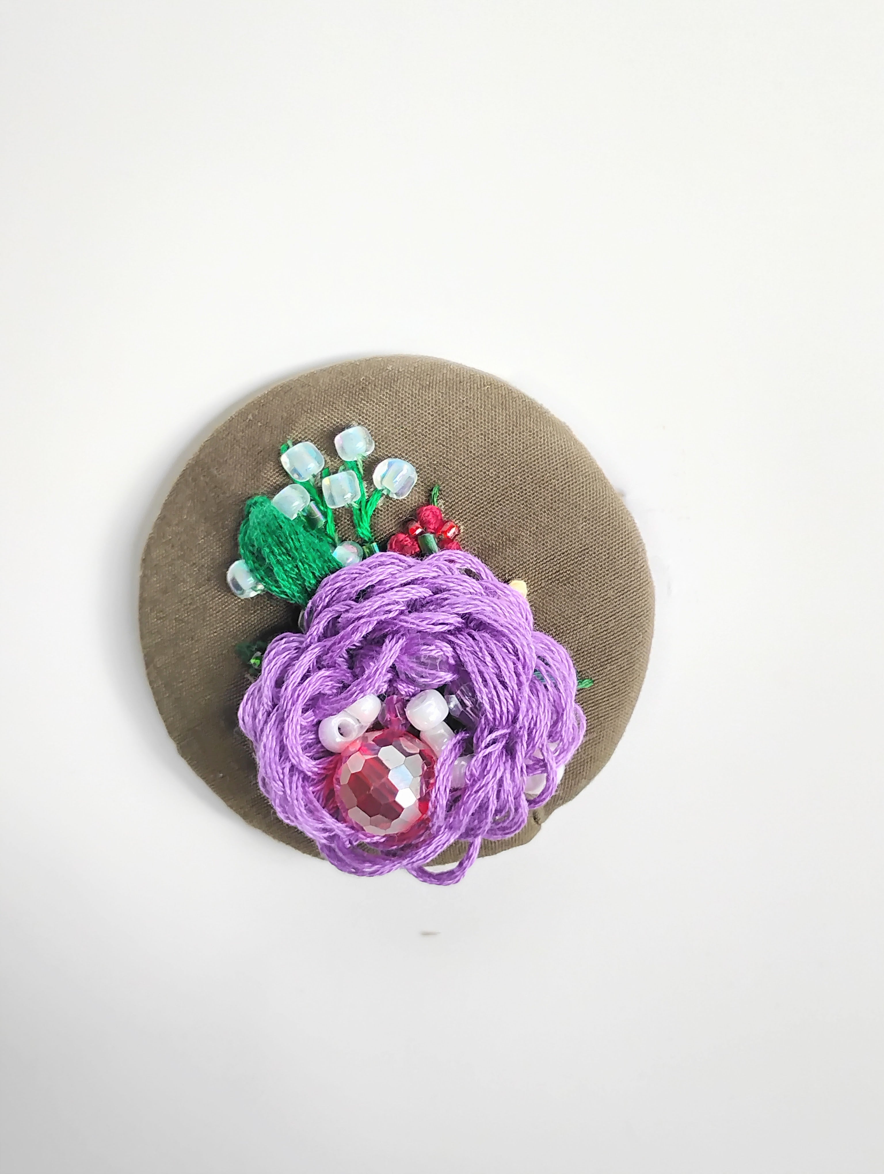 Decorative purple flower brooch on olive background