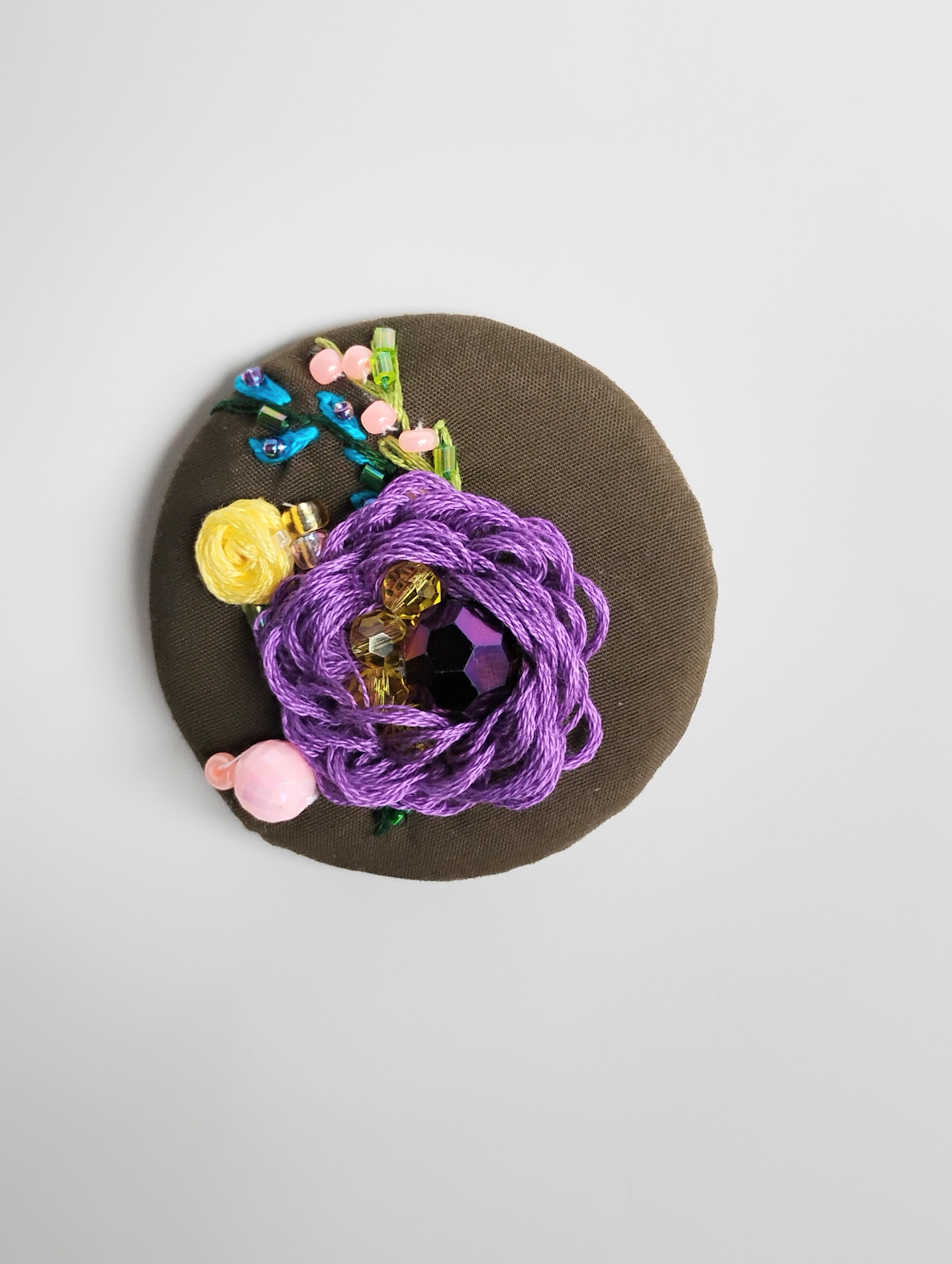 Decorative purple flower brooch on olive background