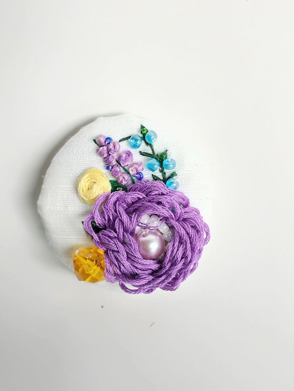 Decorative purple flower brooch on white textured background