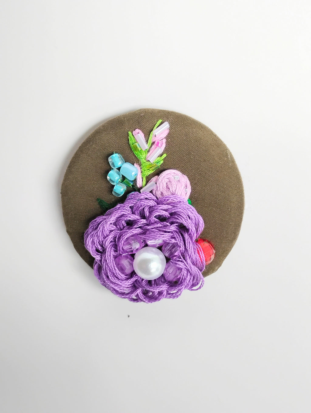 Decorative purple flower brooch on olive background