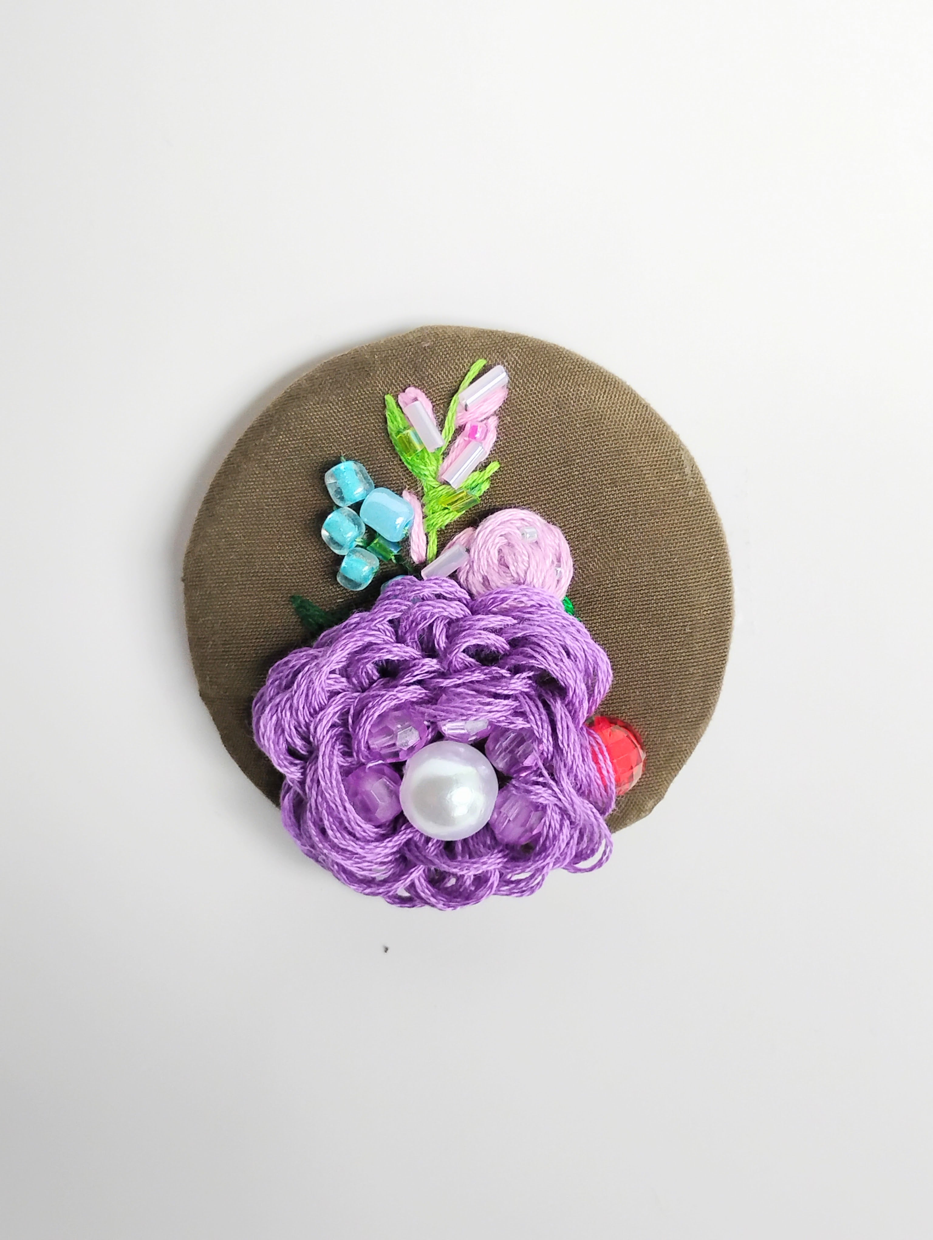 Decorative purple flower brooch on olive background