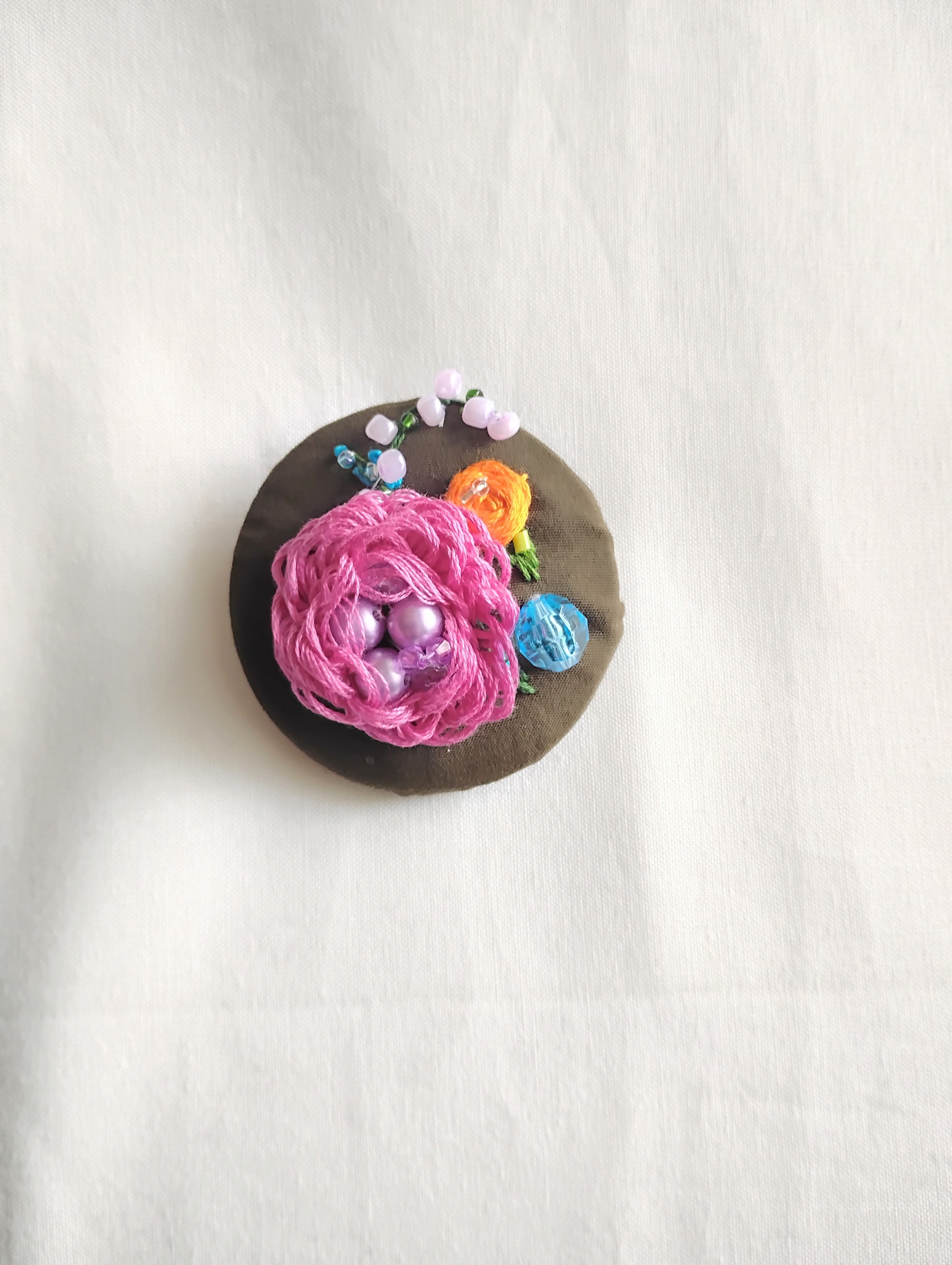 Decorative fuschia flower brooch on olive background