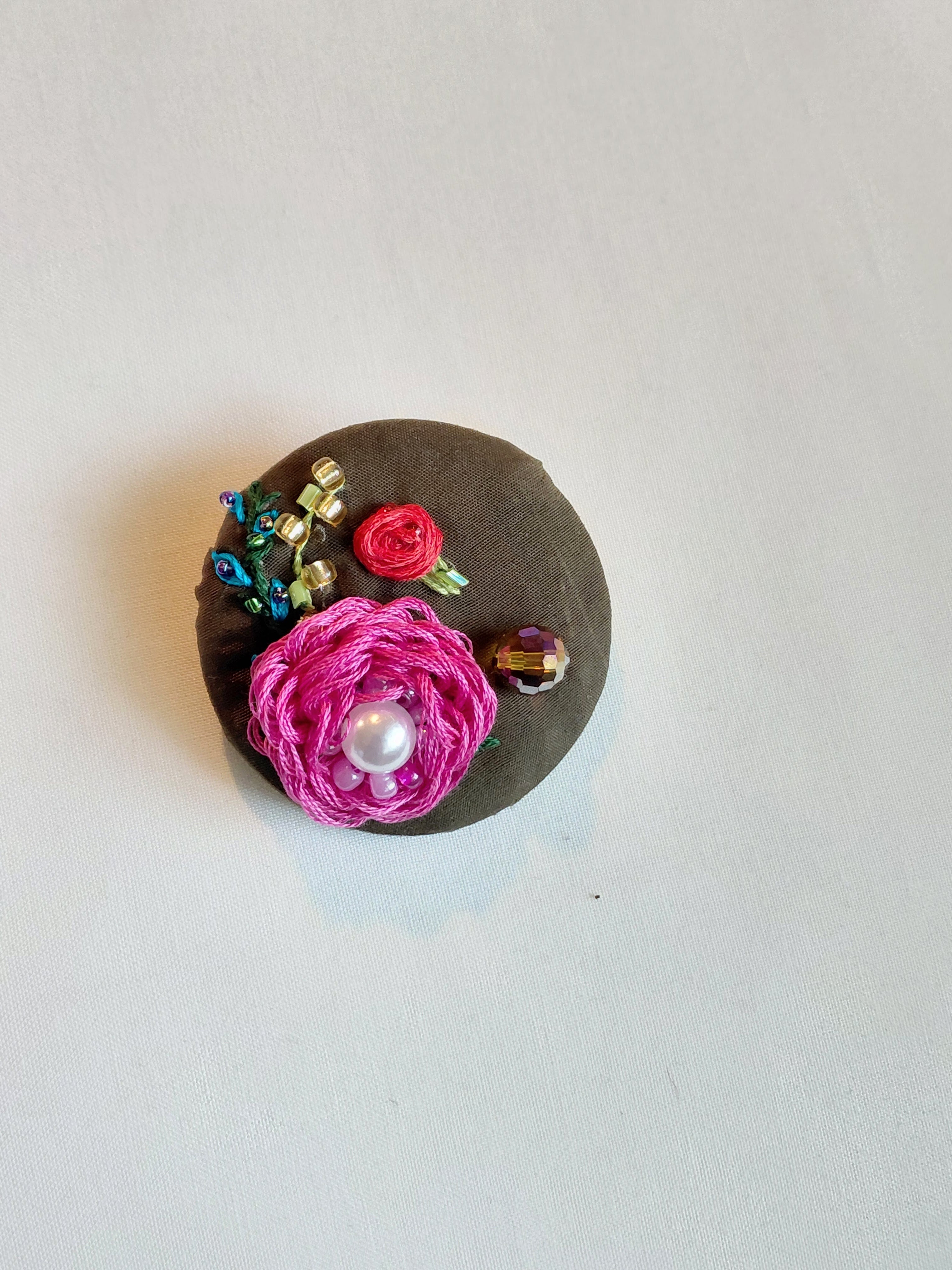 Decorative fuschia flower brooch on olive background