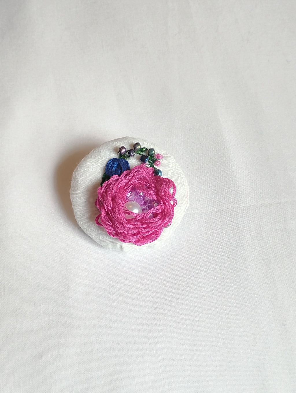 Decorative fuschia flower brooch on white textured background