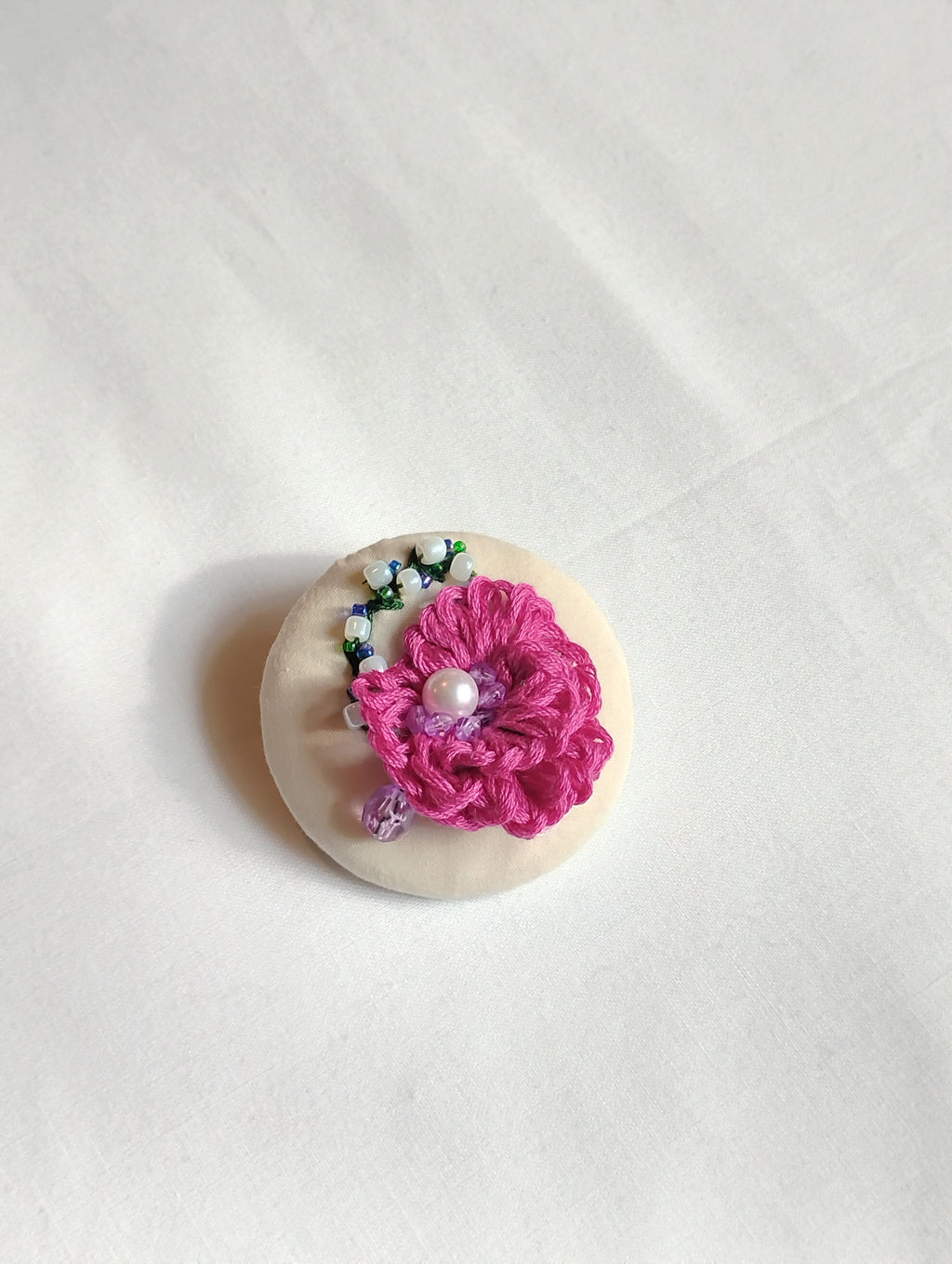 Decorative fuschia flower brooch on white textured background