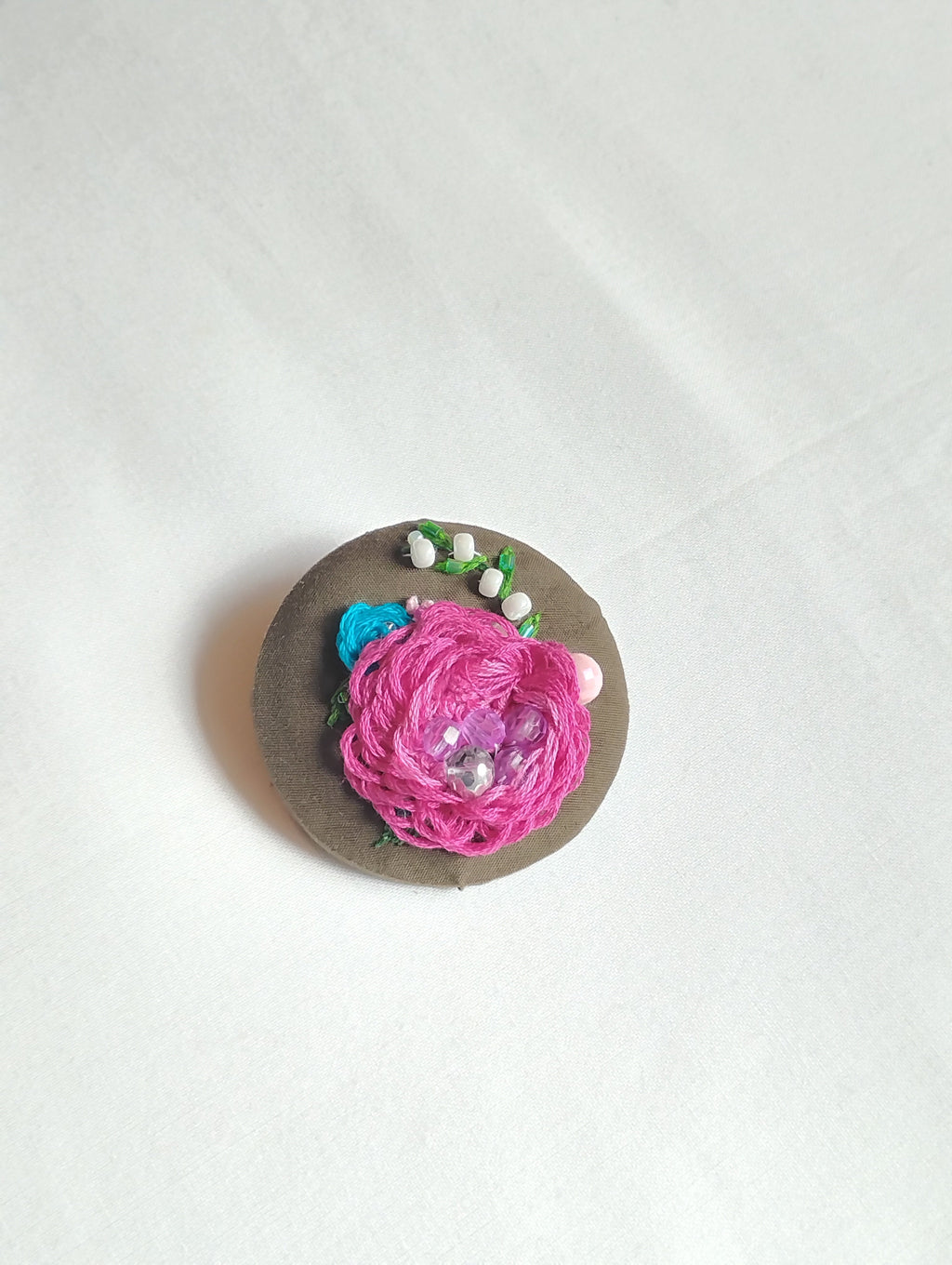 Decorative fuschia flower brooch on olive background