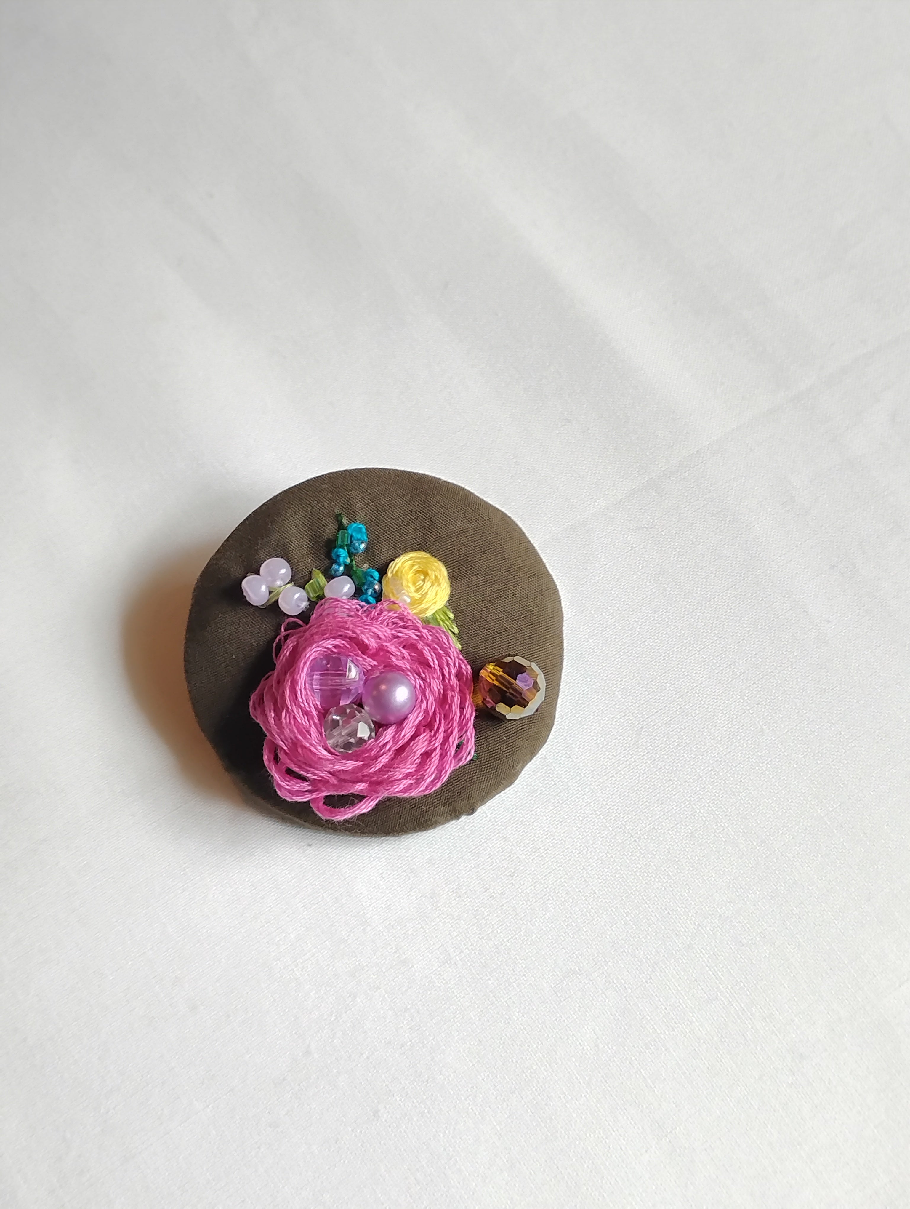 Decorative fuschia flower brooch on olive background
