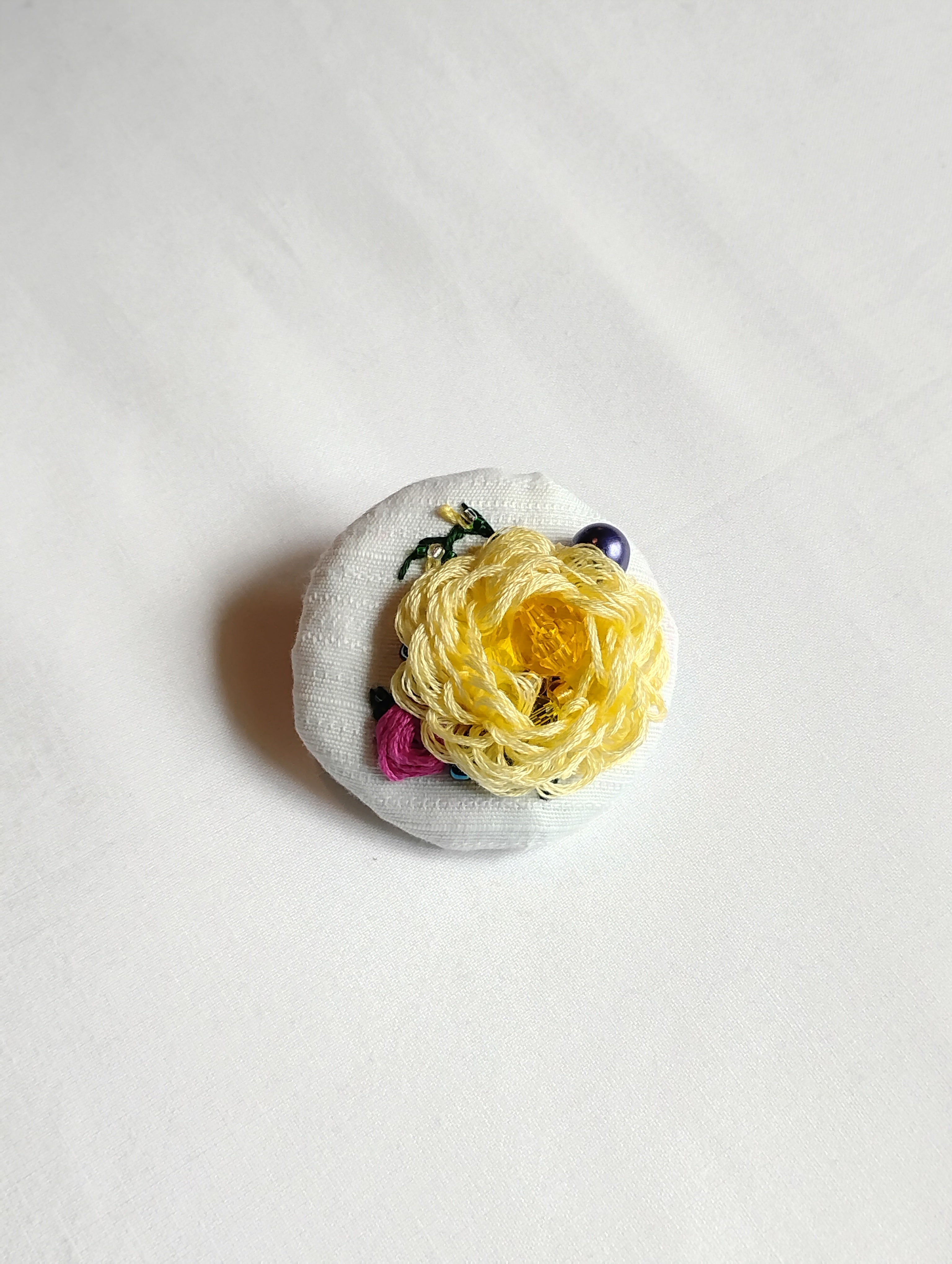 Decorative yellow flower brooch on white textured background