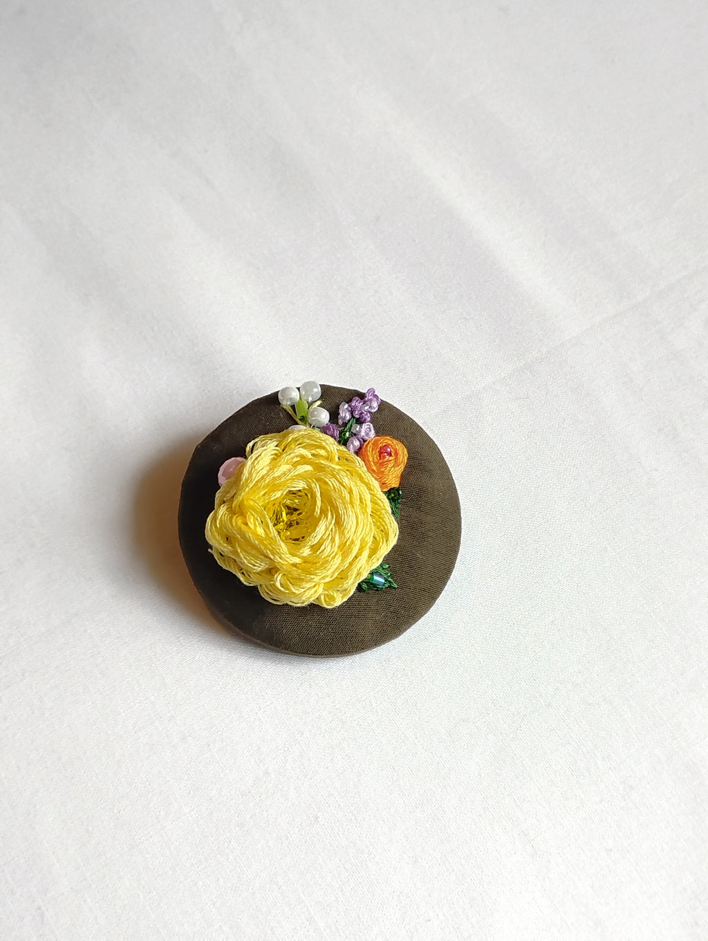 Decorative yellow flower brooch on olive background
