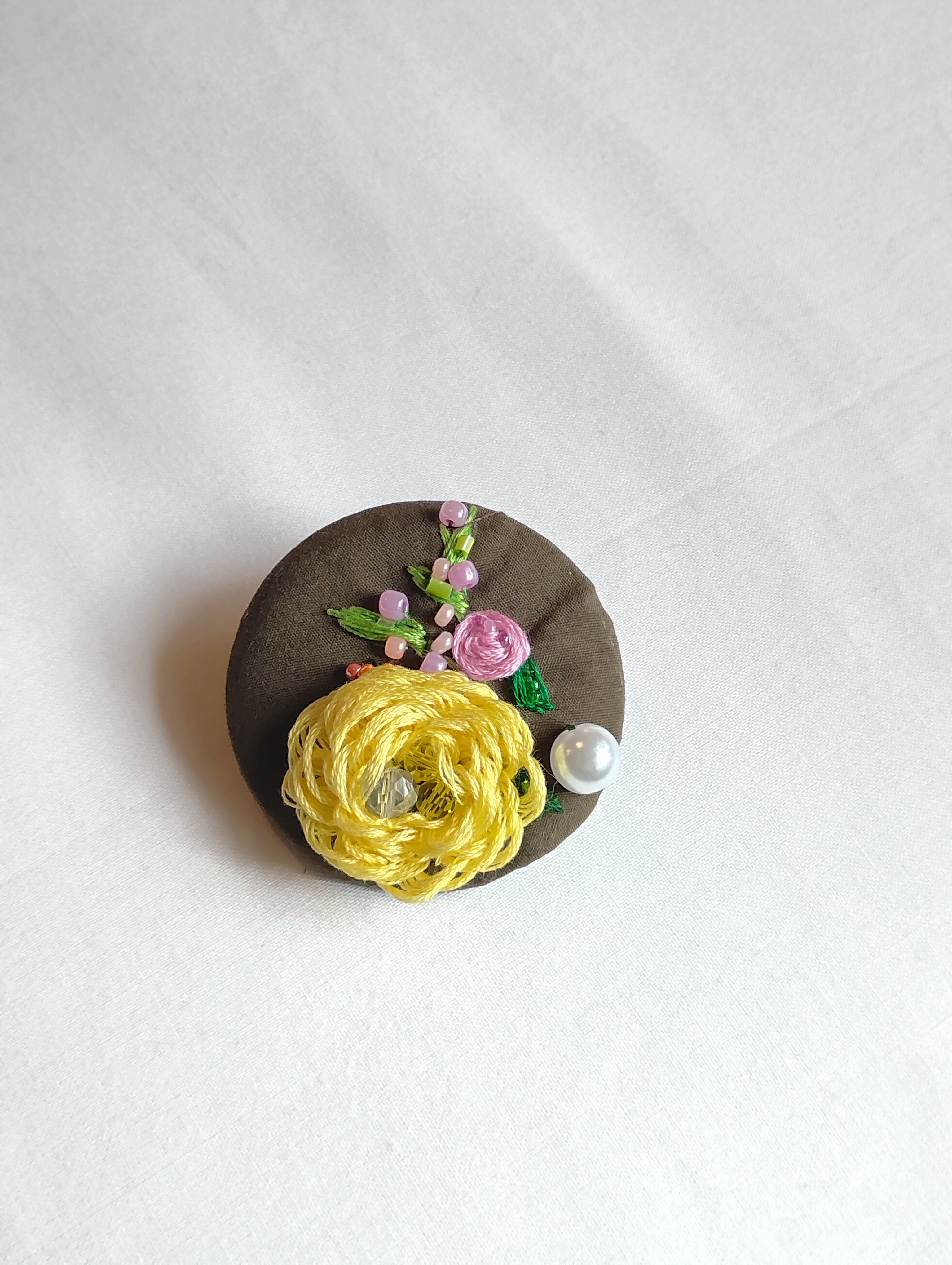 Decorative yellow flower brooch on olive background