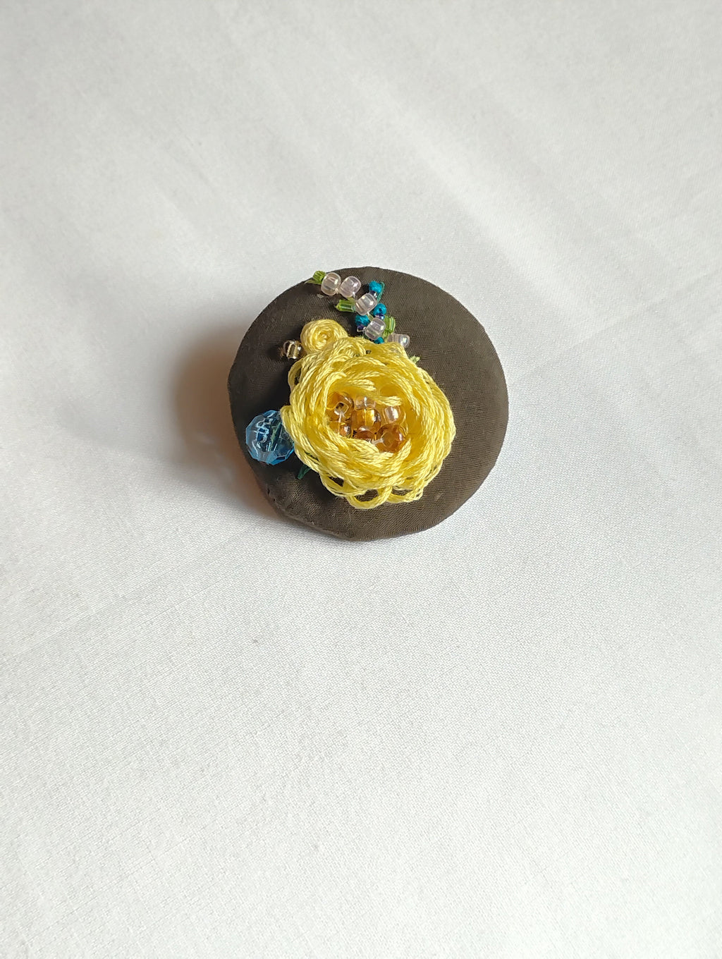 Decorative yellow flower brooch on olive background