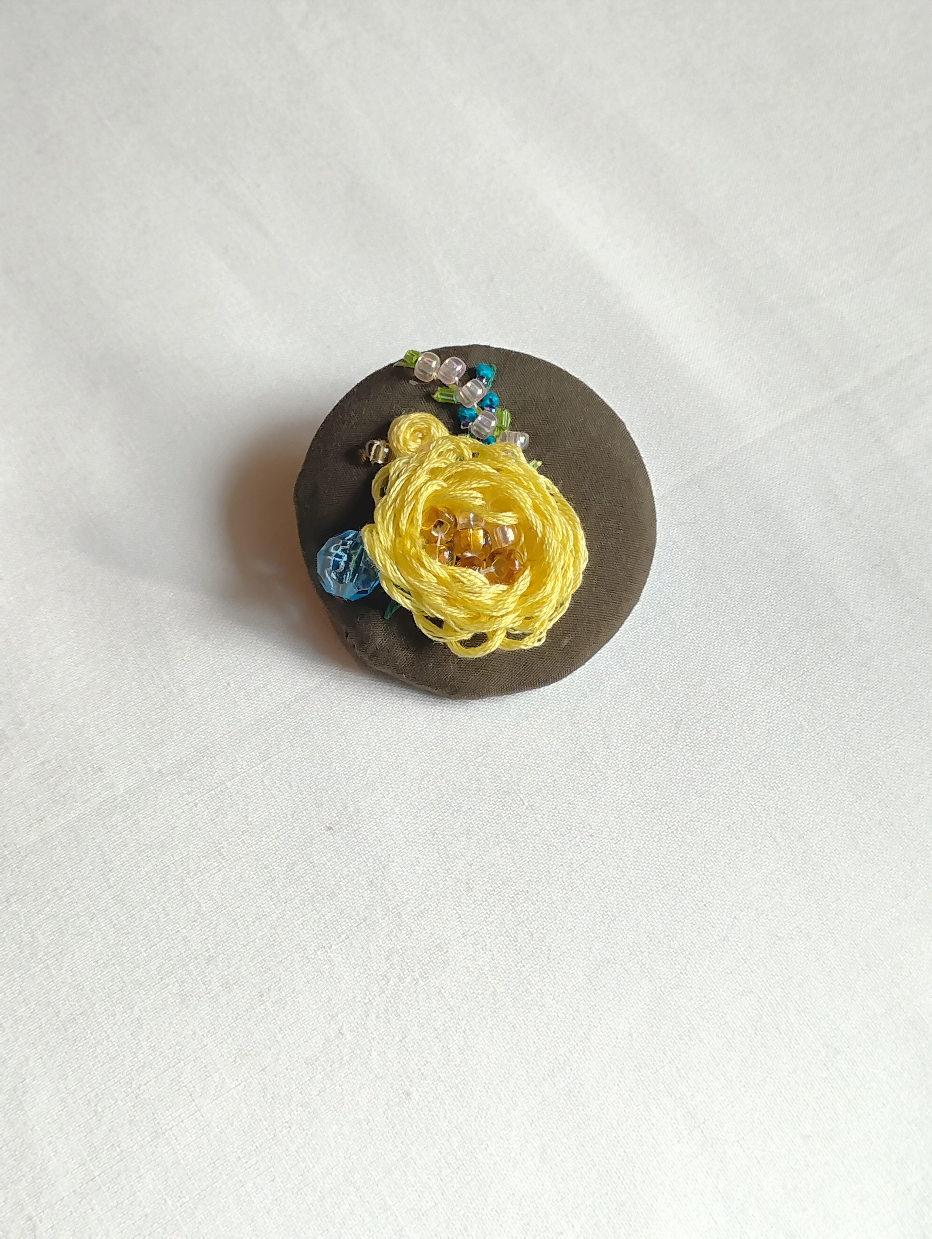Decorative yellow flower brooch on olive background