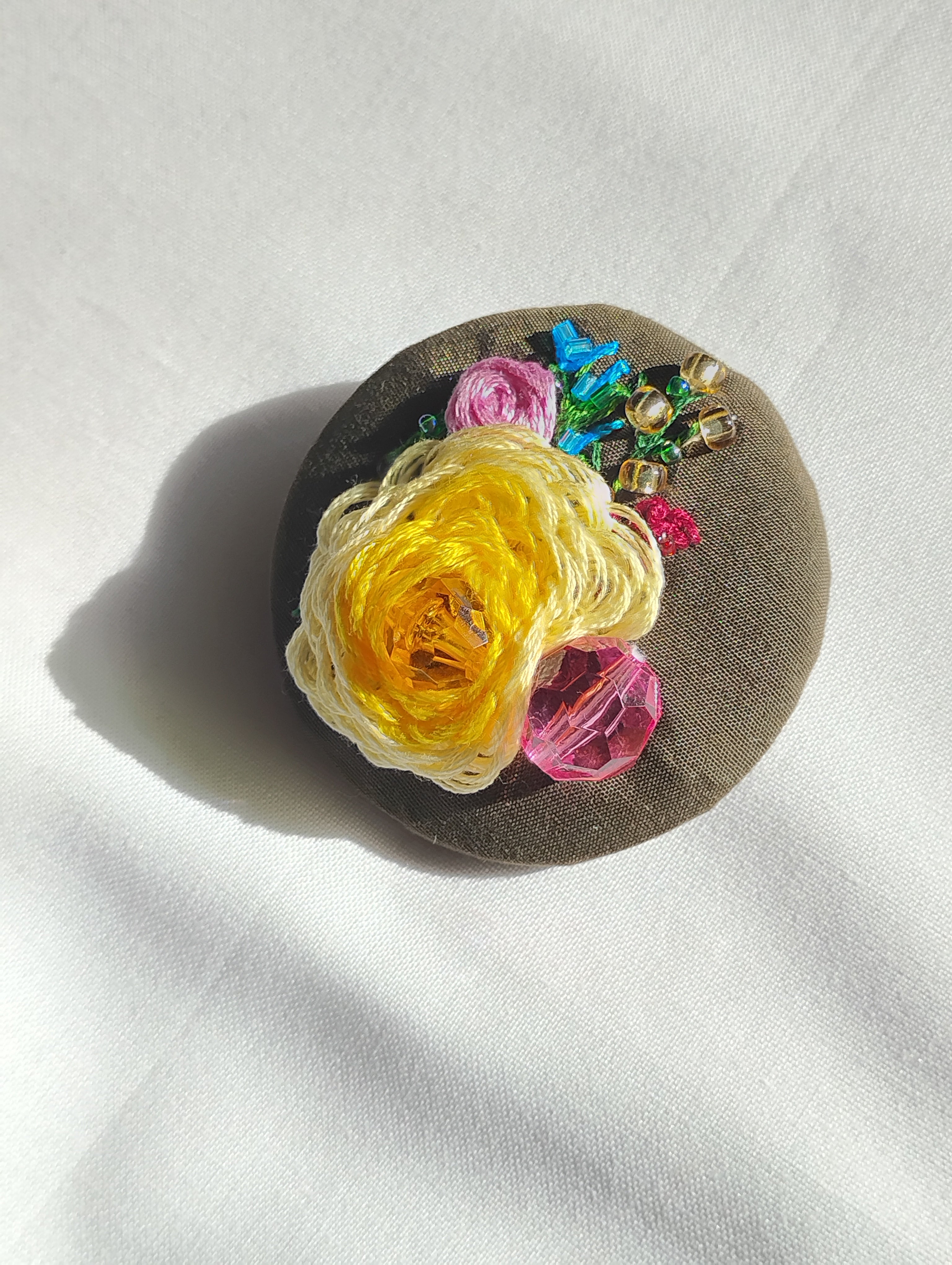 Decorative yellow flower brooch on olive background