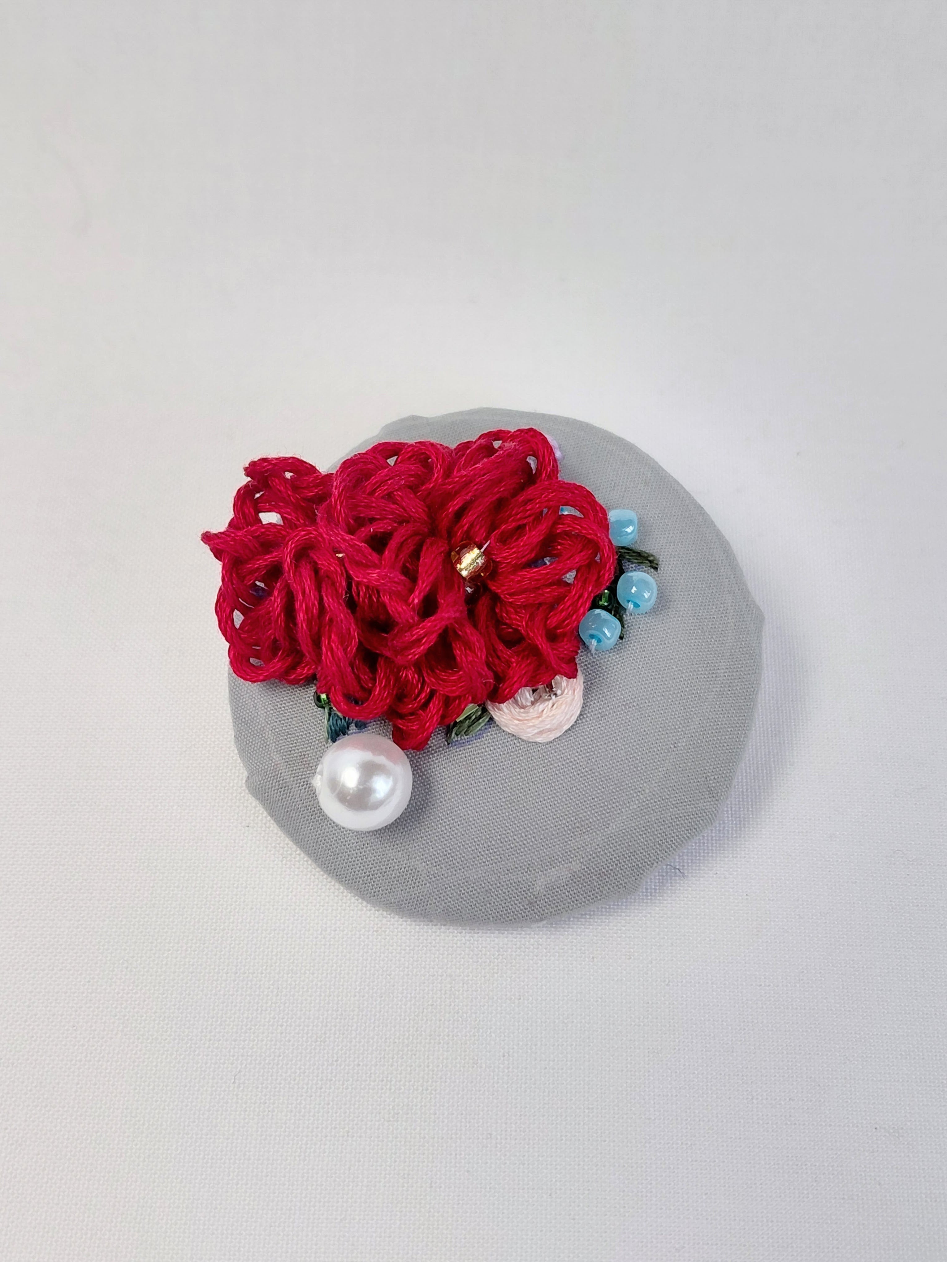 Decorative burgundy flower brooch on grey background
