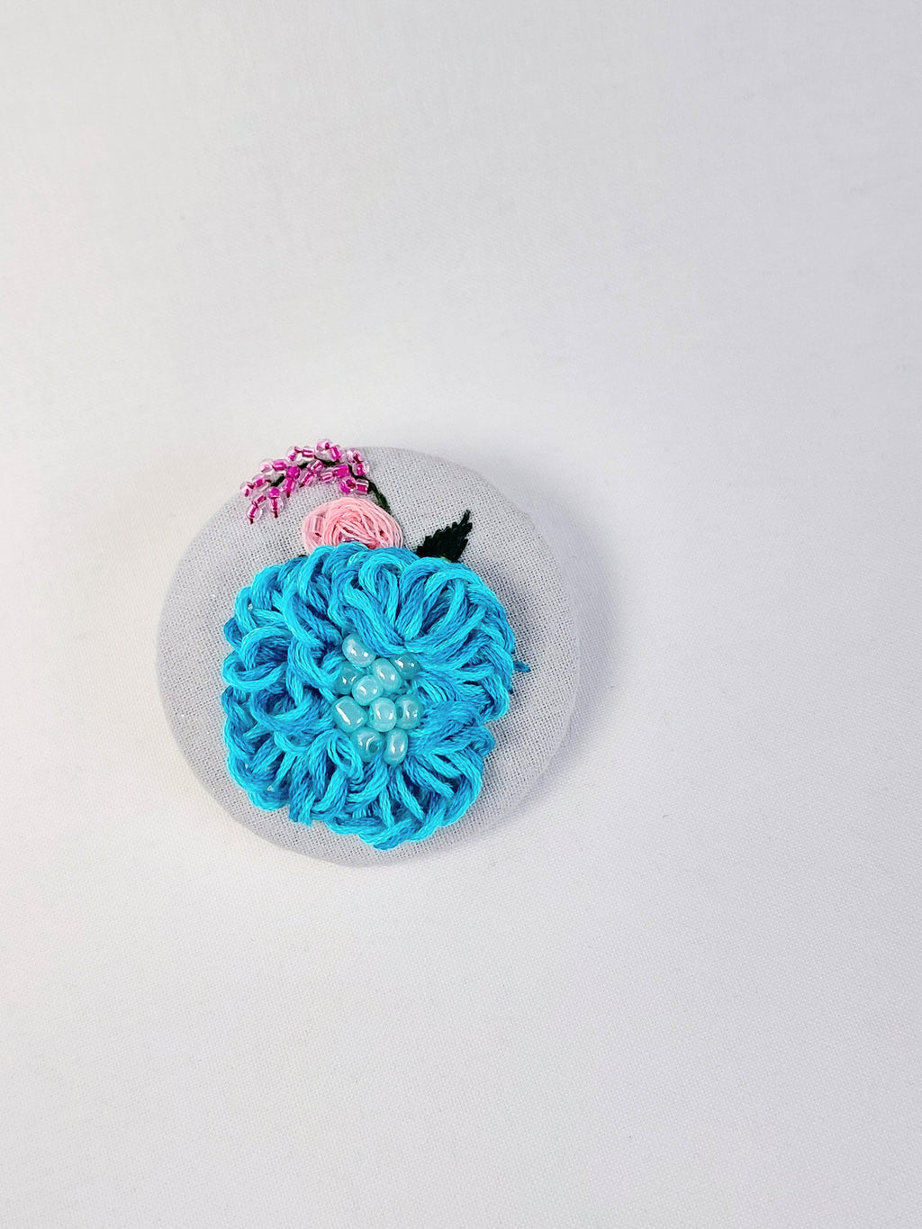 Decorative turquoise flower brooch on light blue with specs background