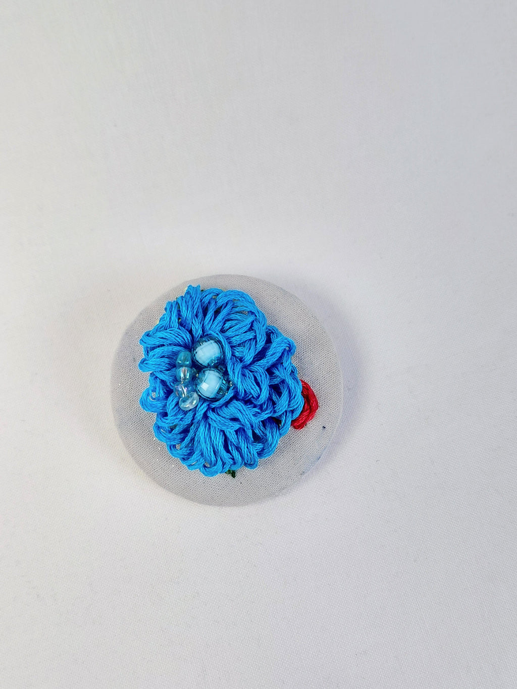 Decorative turquoise flower brooch on light blue with specs background
