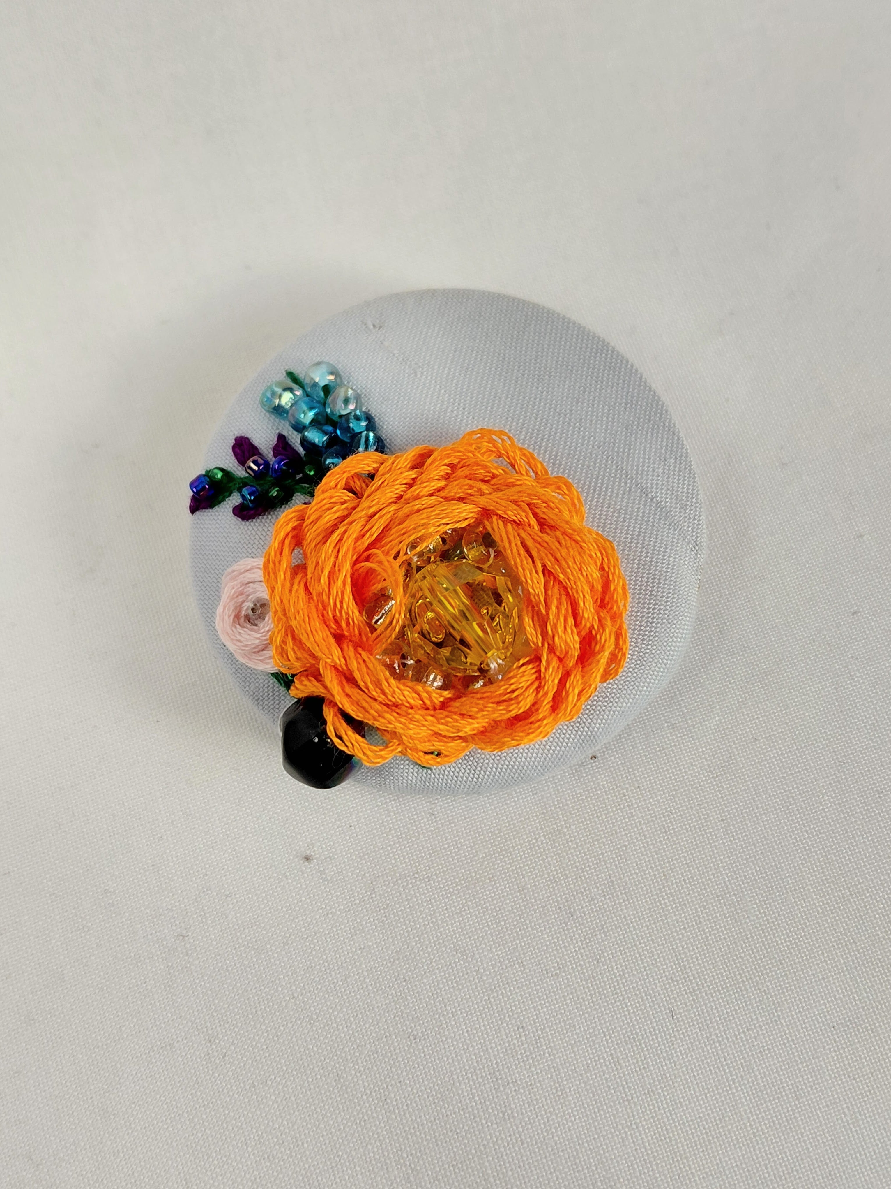 Decorative orange flower brooch on light blue background