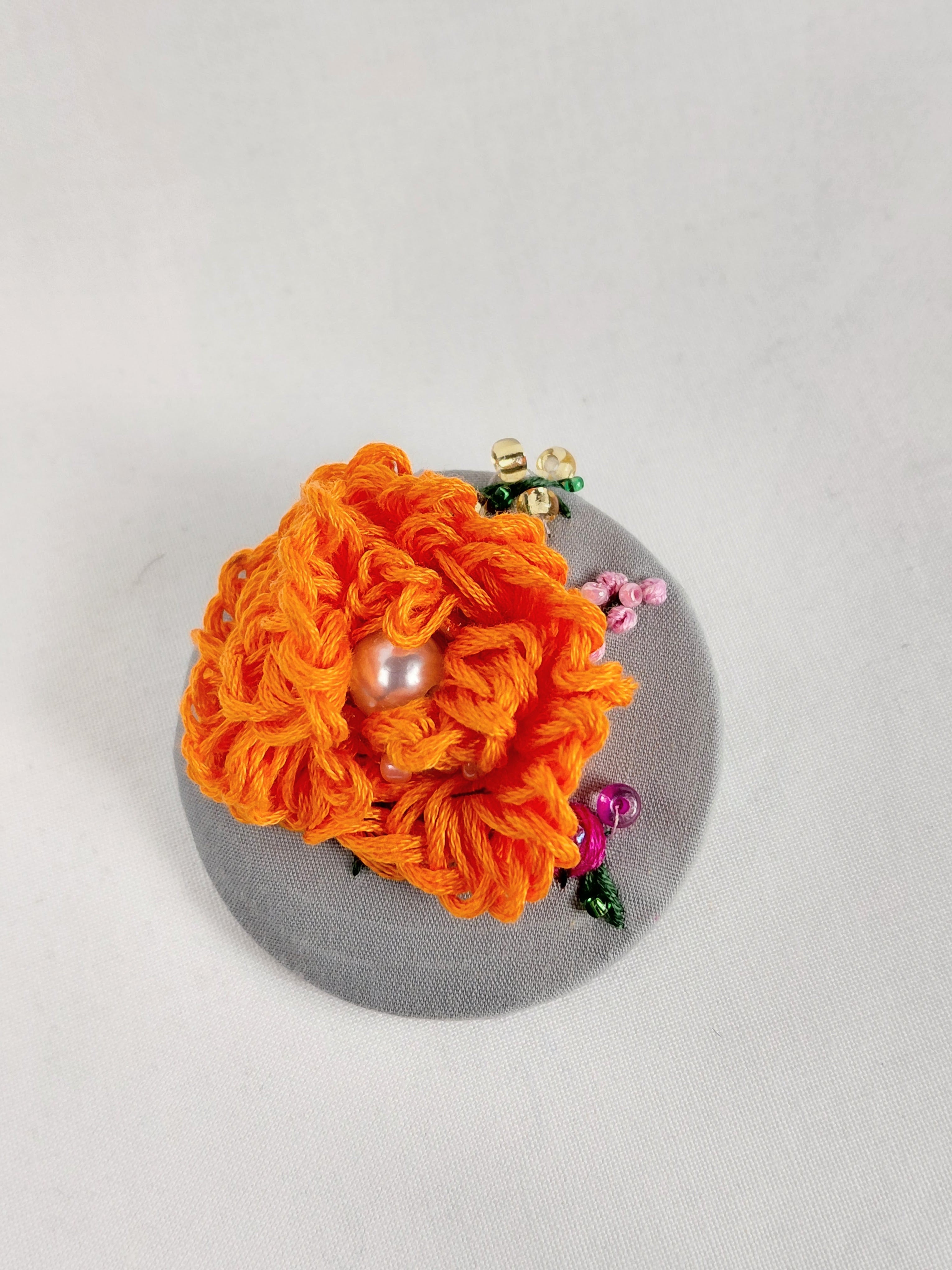 Decorative orange flower brooch on grey background