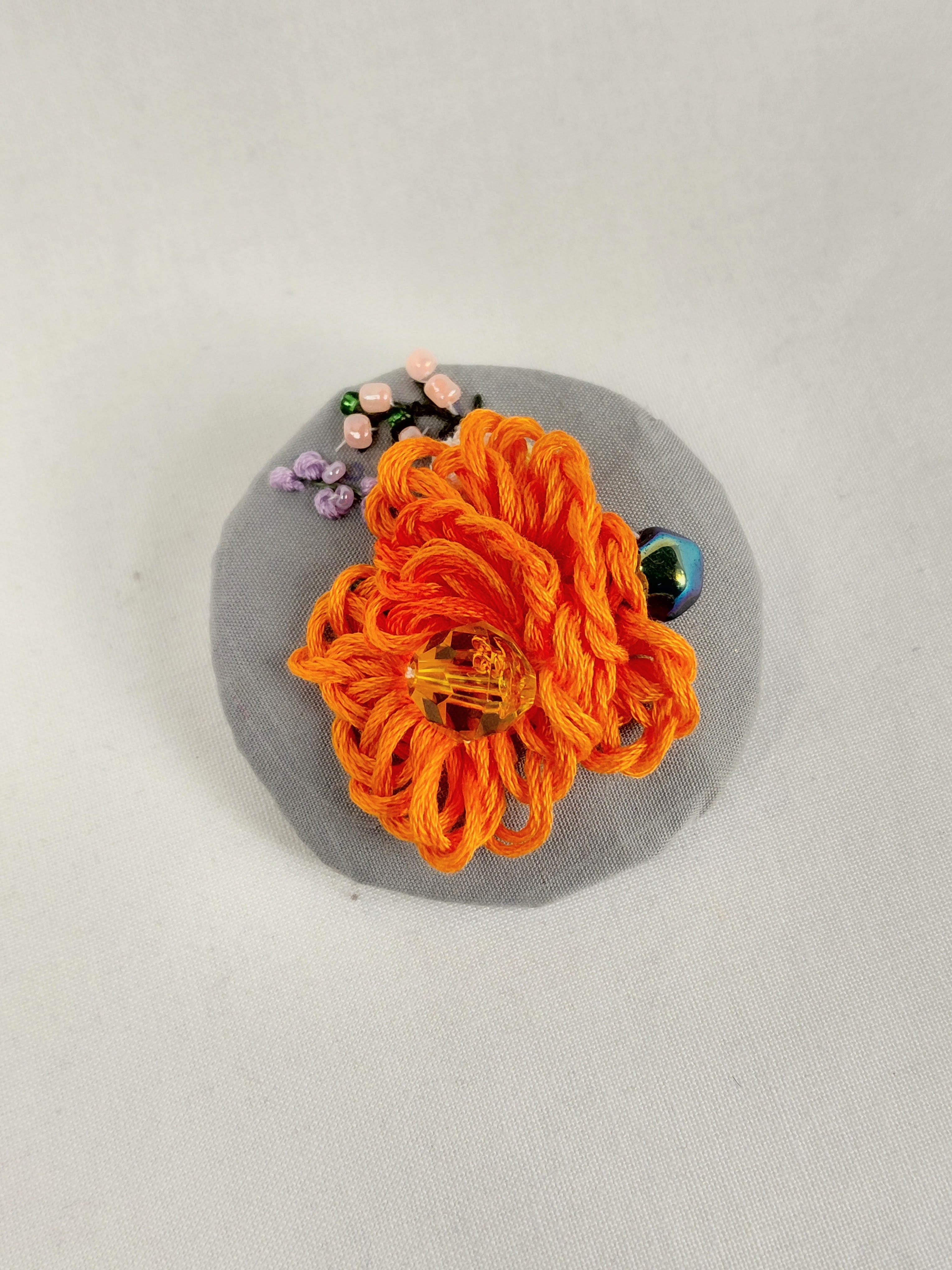 Decorative orange flower brooch on grey background