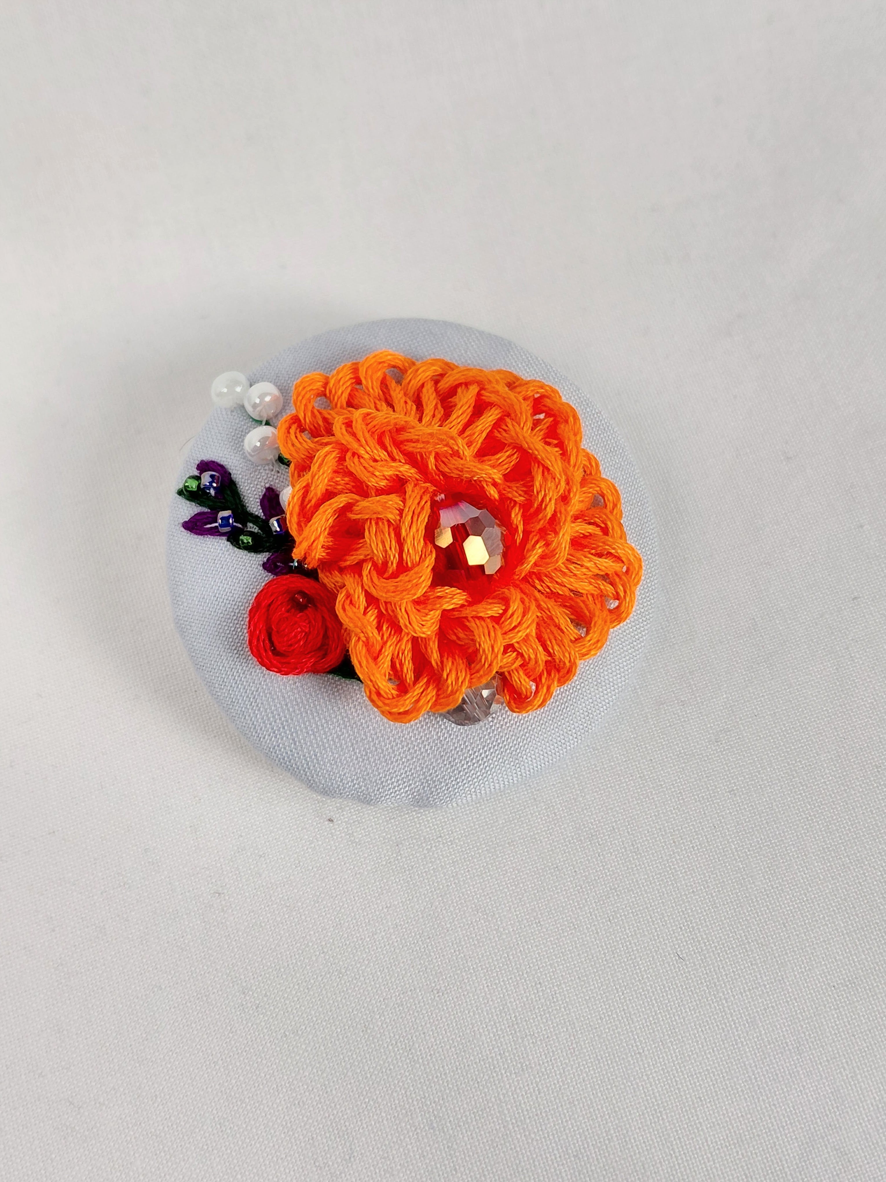 Decorative orange flower brooch on light blue background