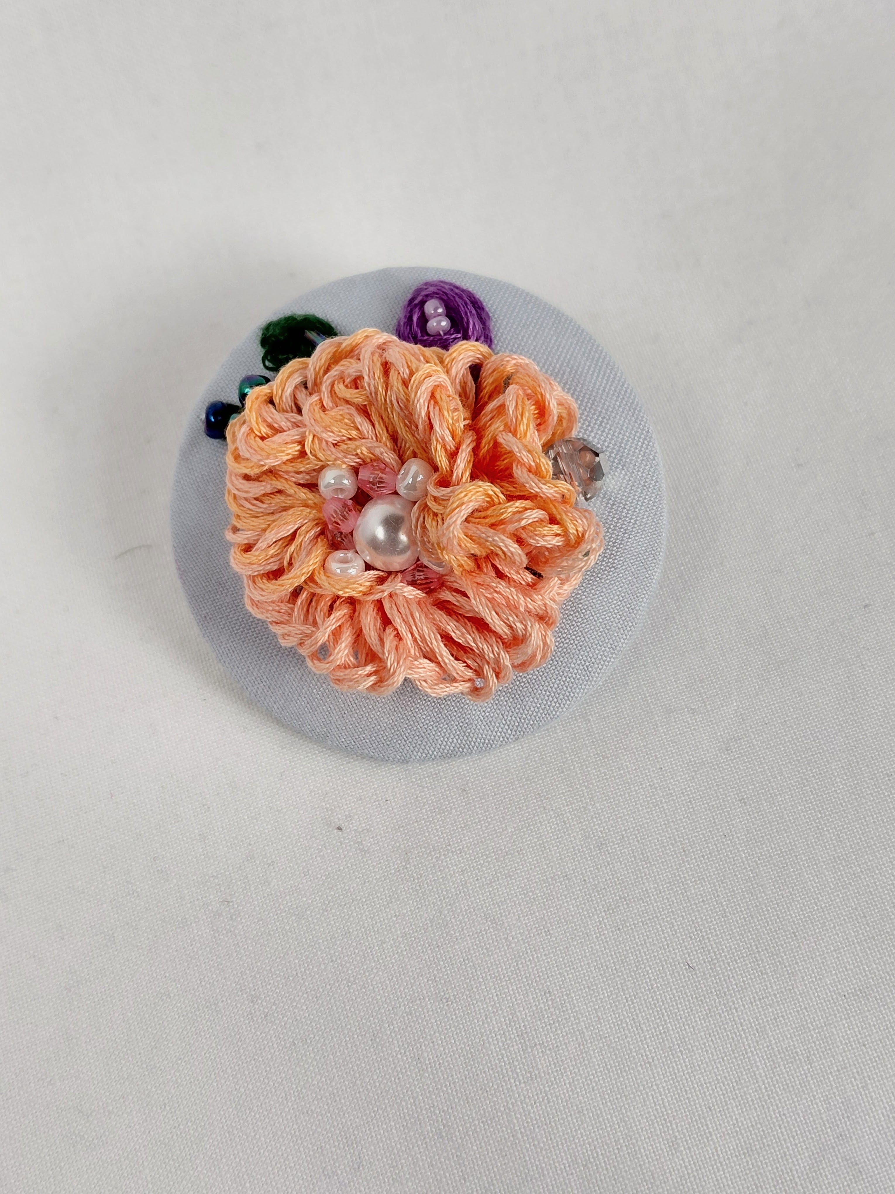 Decorative orange flower brooch on light blue background