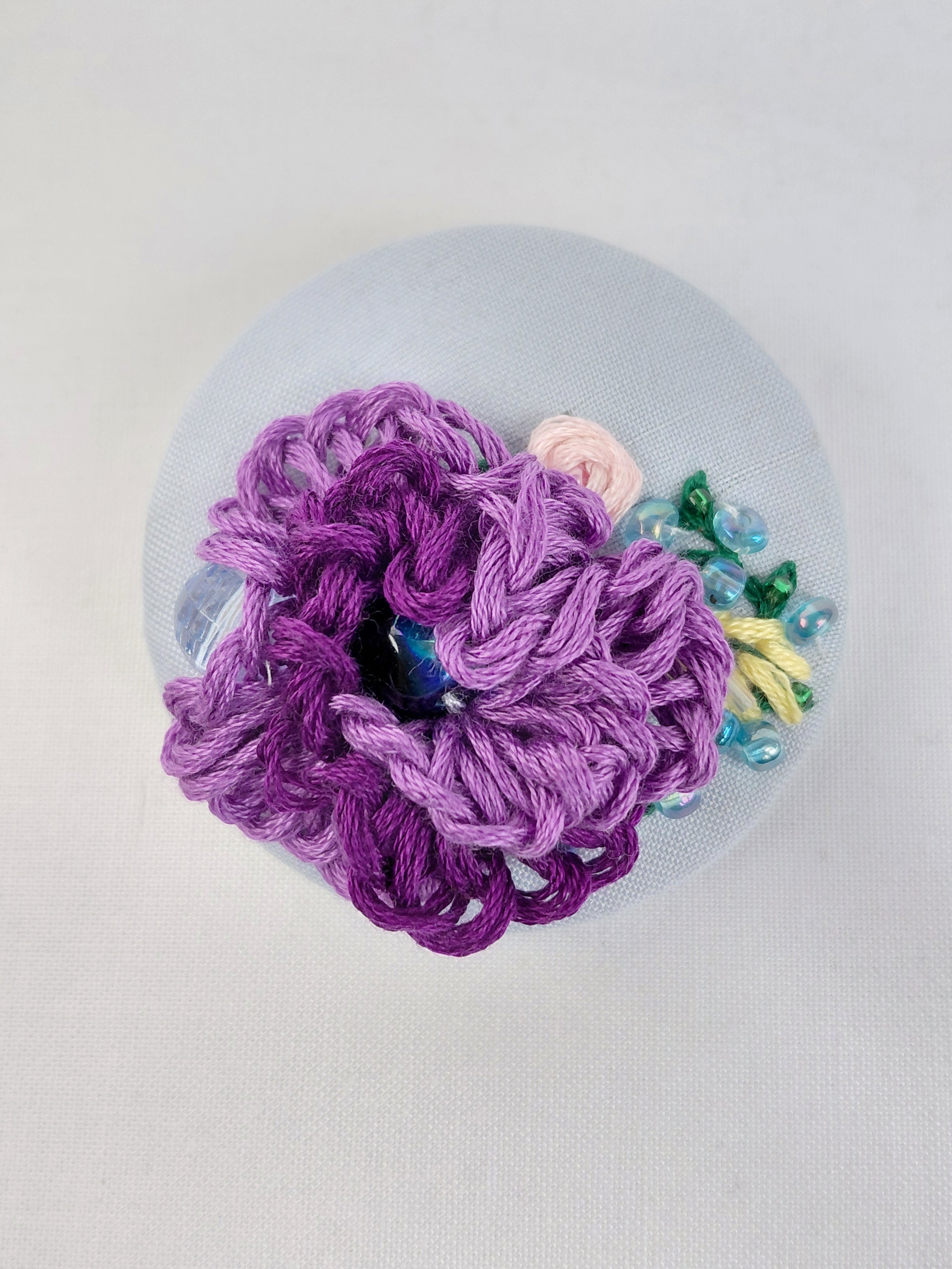 Decorative purple flower brooch on light blue background