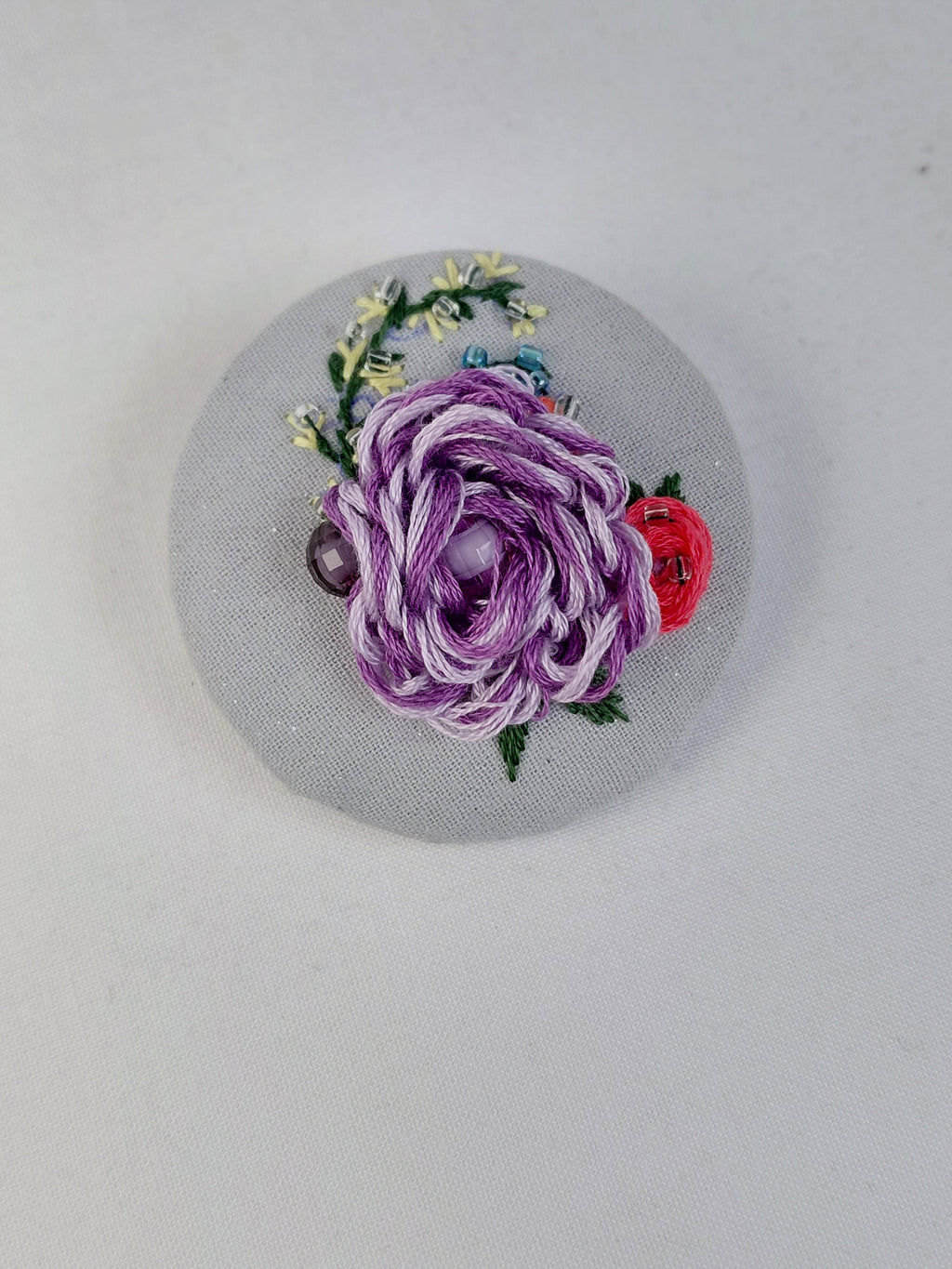 Decorative purple flower brooch on light blue with specs background