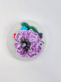Decorative purple flower brooch on grey with specs background