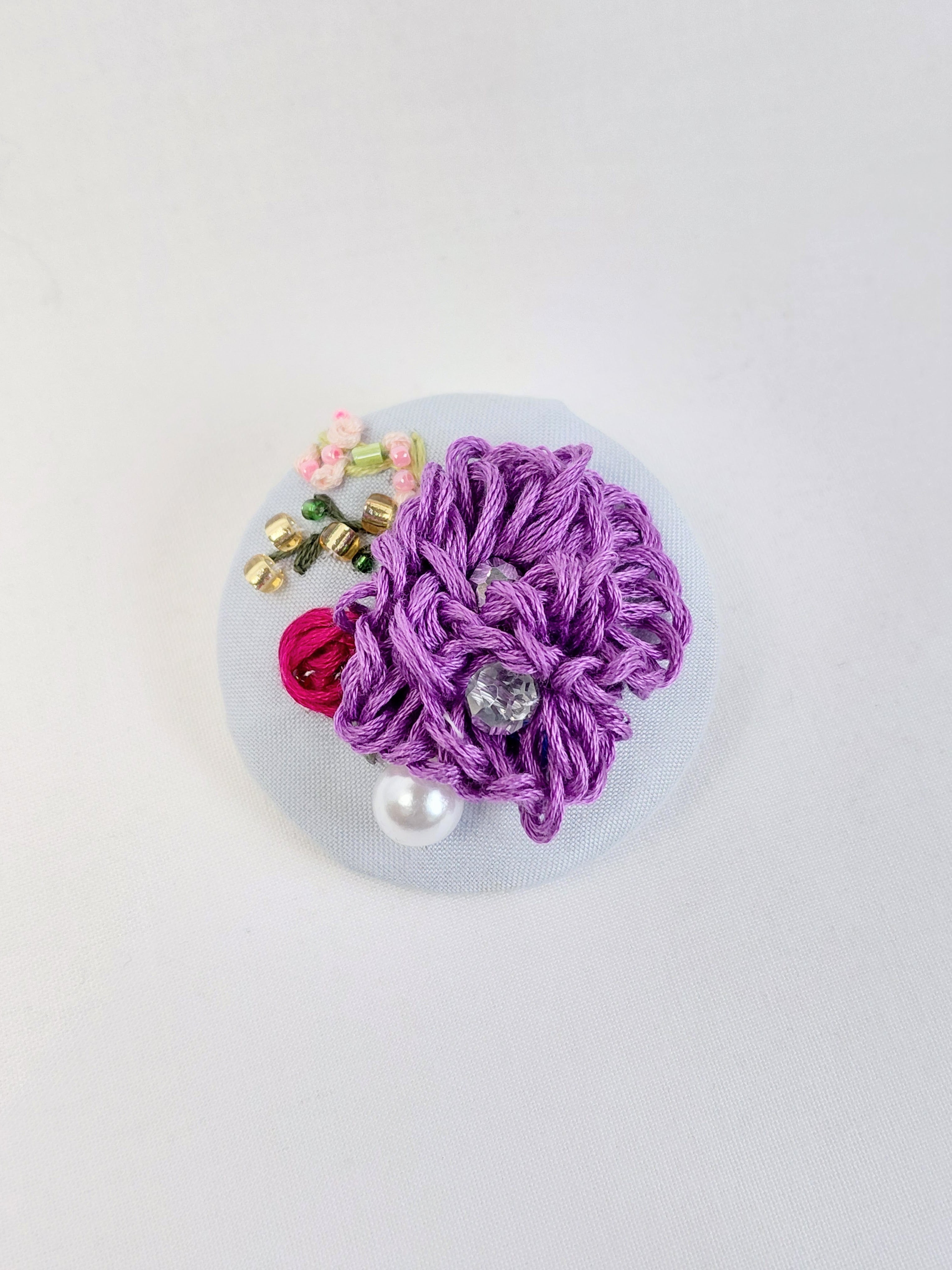 Decorative purple flower brooch on light blue background