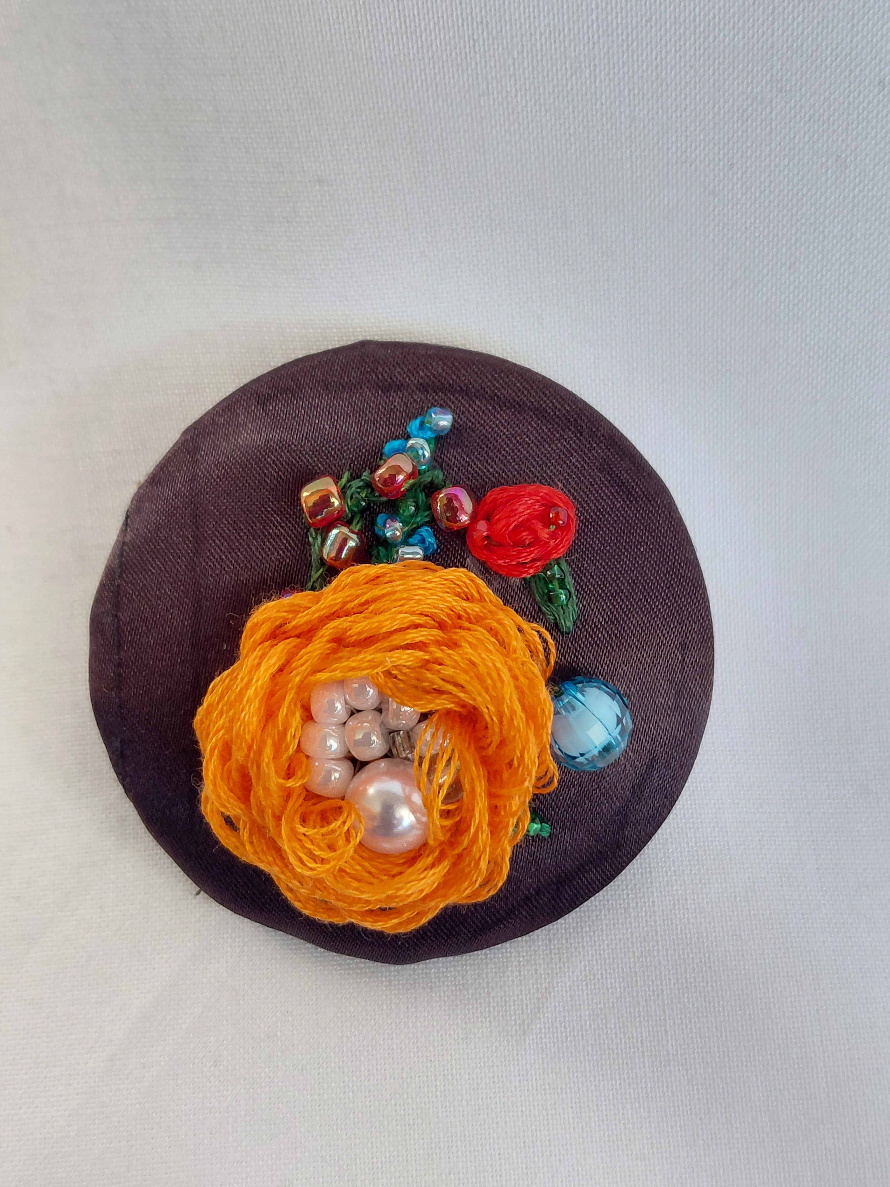Decorative orange flower brooch on brown background