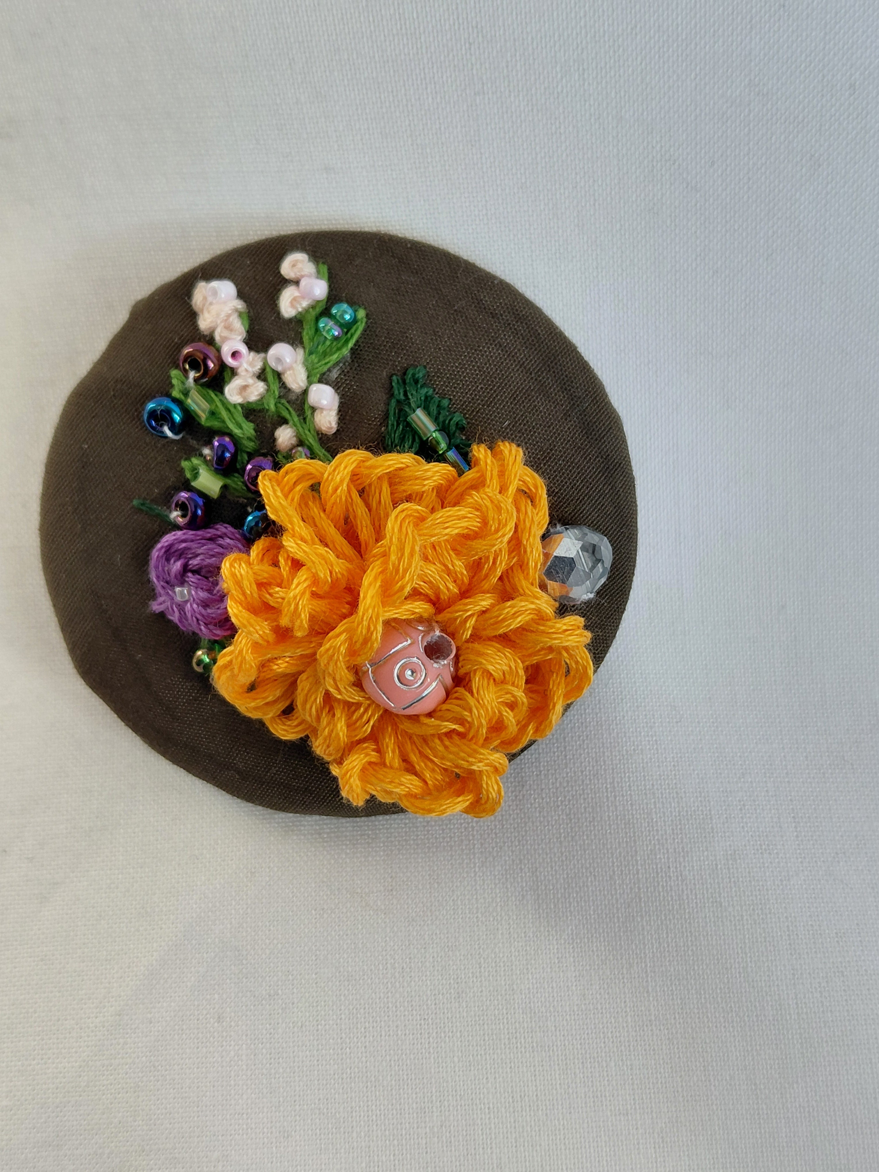 Decorative orange flower brooch on olive background