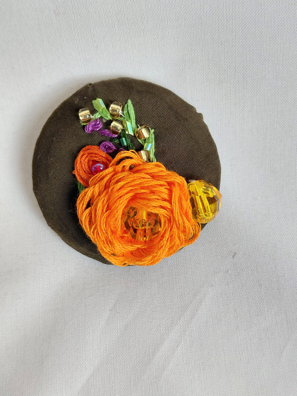 Decorative orange flower brooch on olive background
