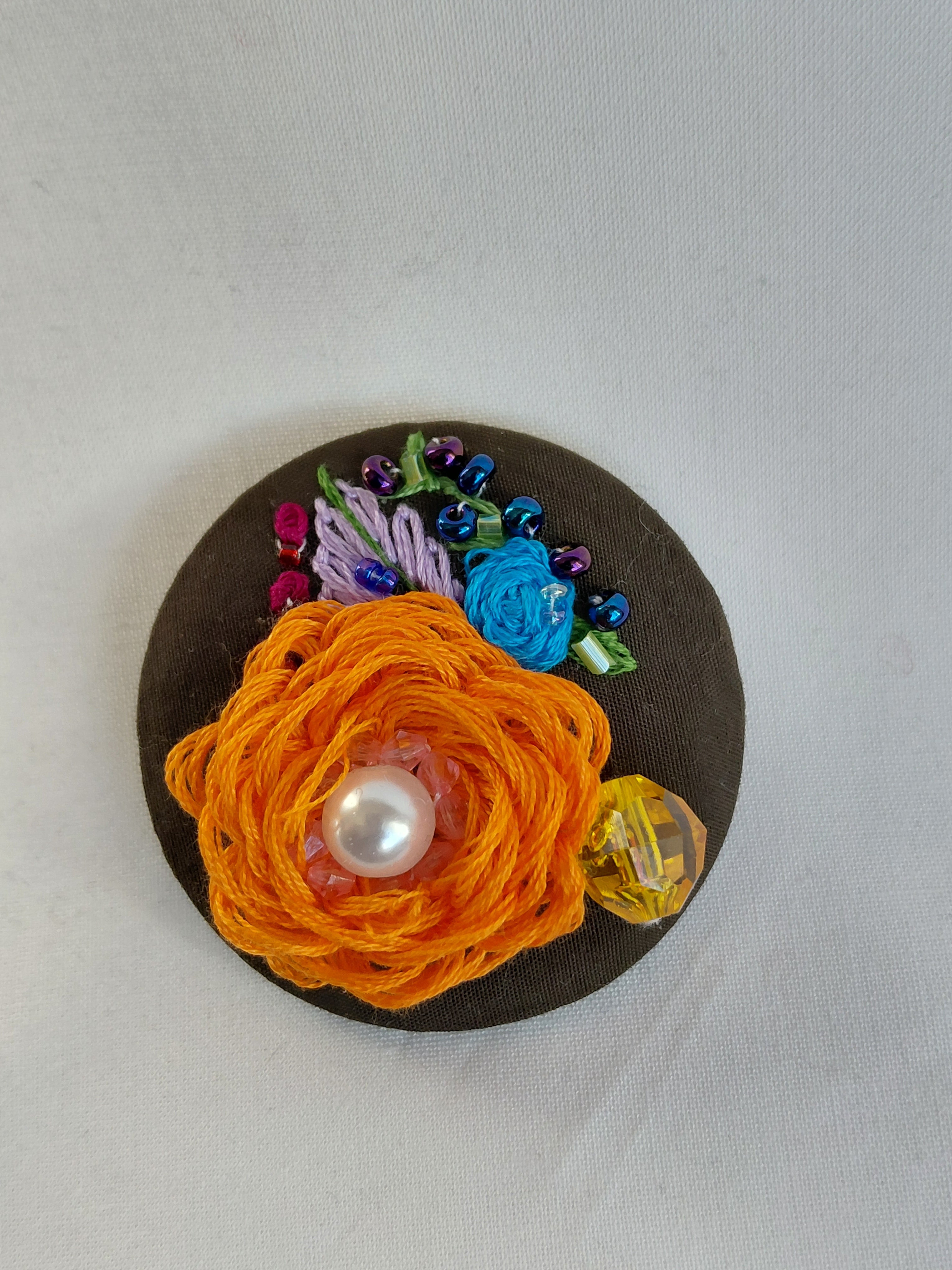 Decorative orange flower brooch on olive background