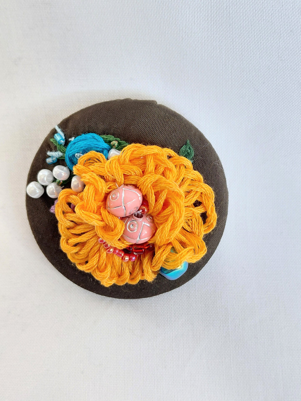 Decorative orange flower brooch on olive background