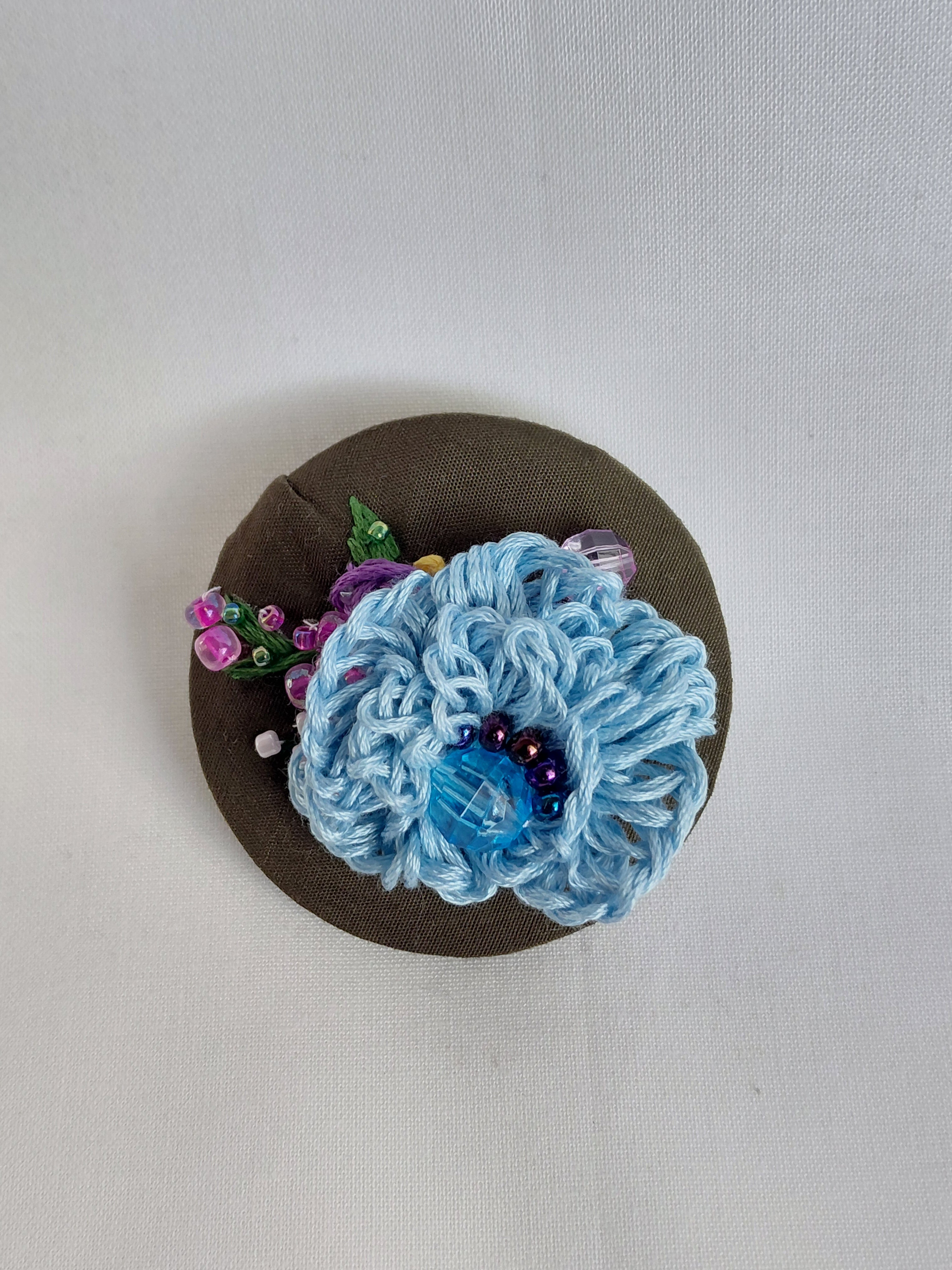 Decorative blue flower brooch on olive background