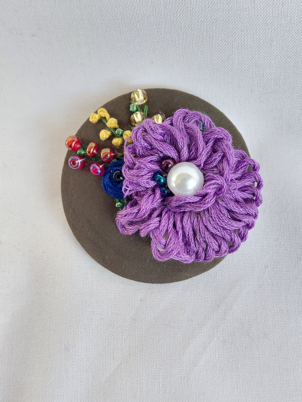Decorative purple flower brooch on olive background