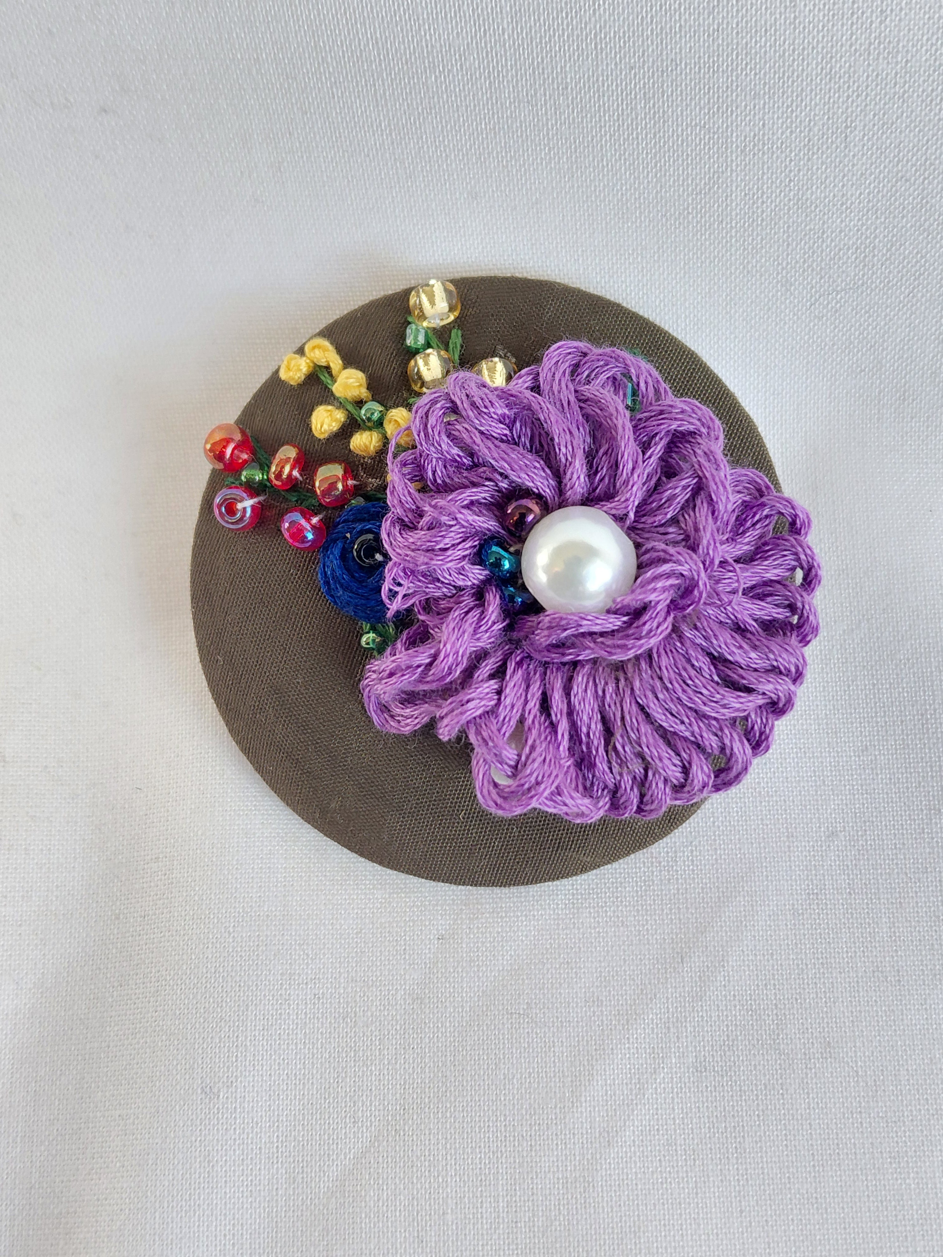 Decorative purple flower brooch on olive background
