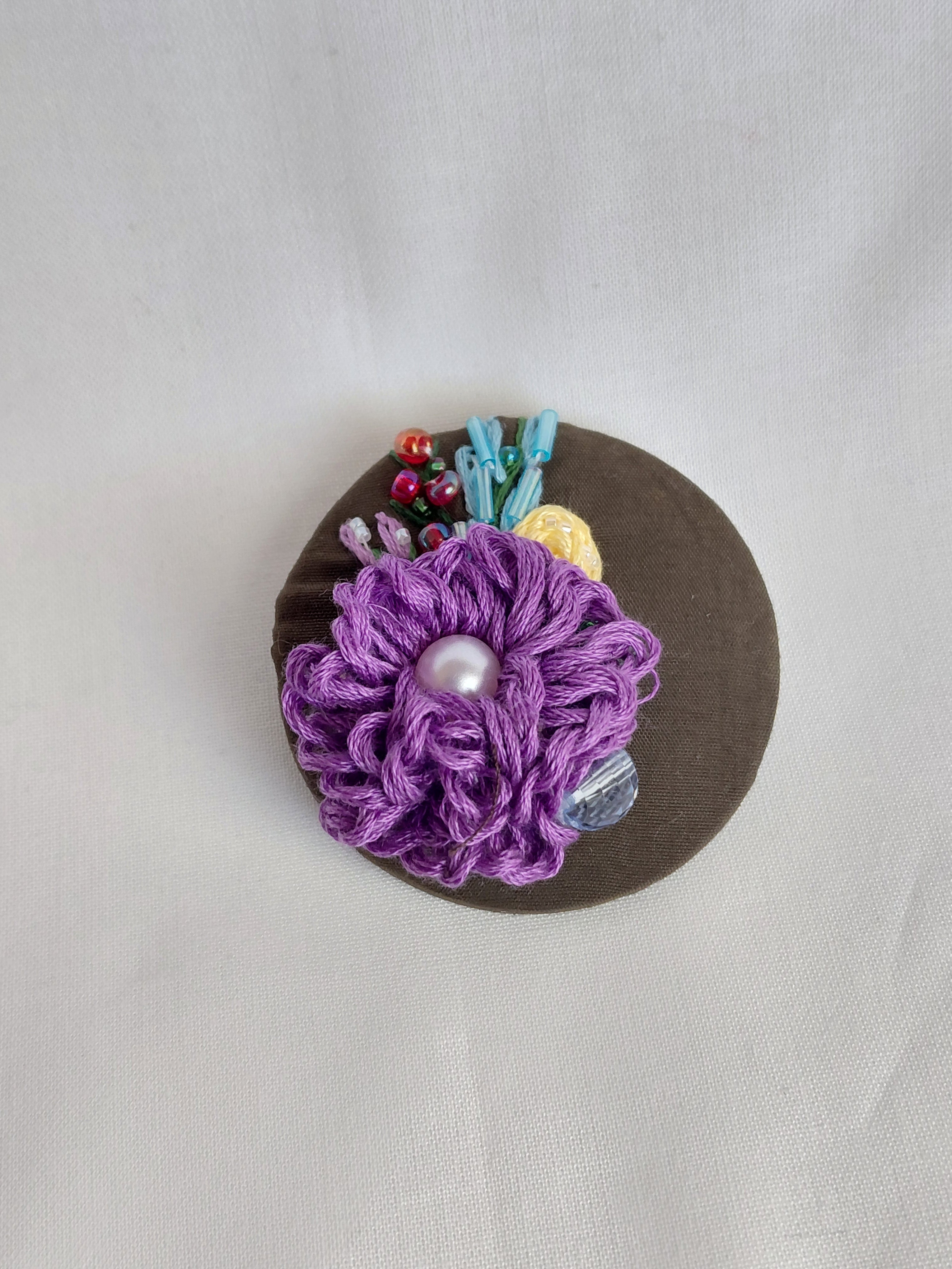 Decorative purple flower brooch on olive background